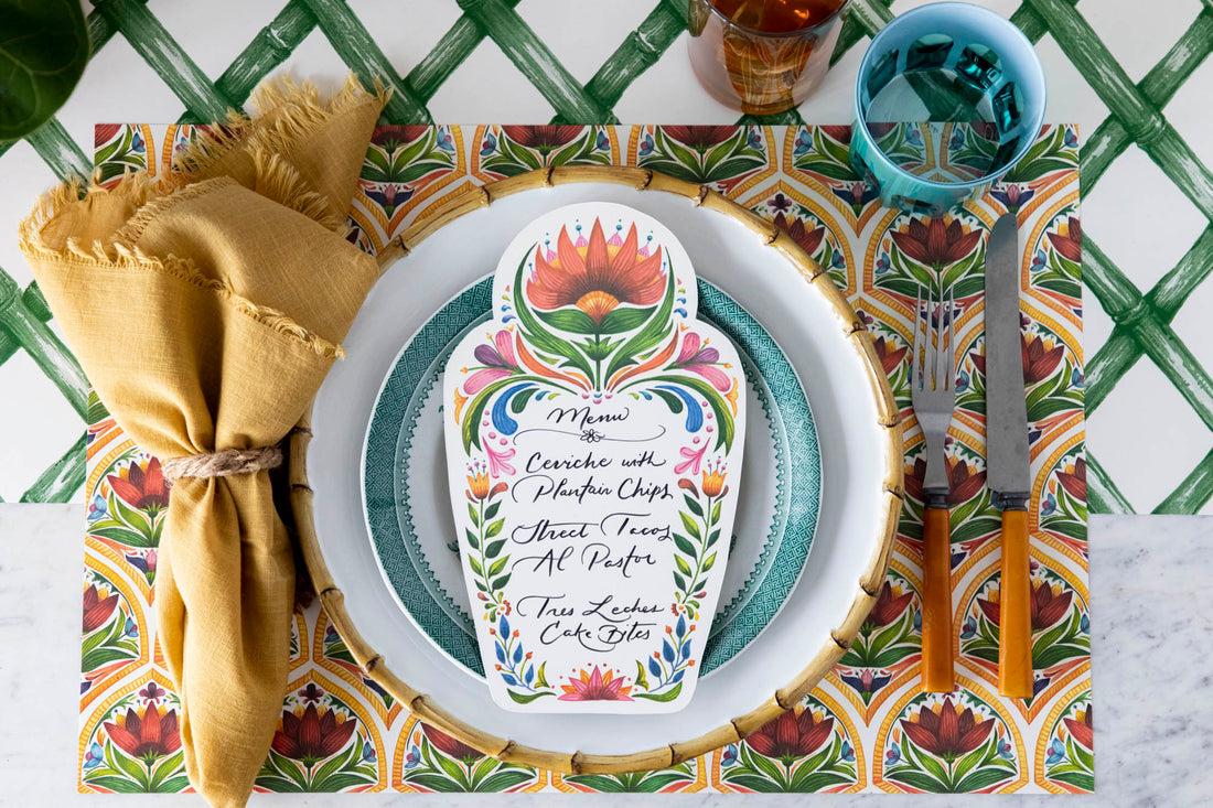 A vibrant place setting featuring a Fiesta Floral Table Card with a menu written on it in beautiful script resting on the plate, from above.