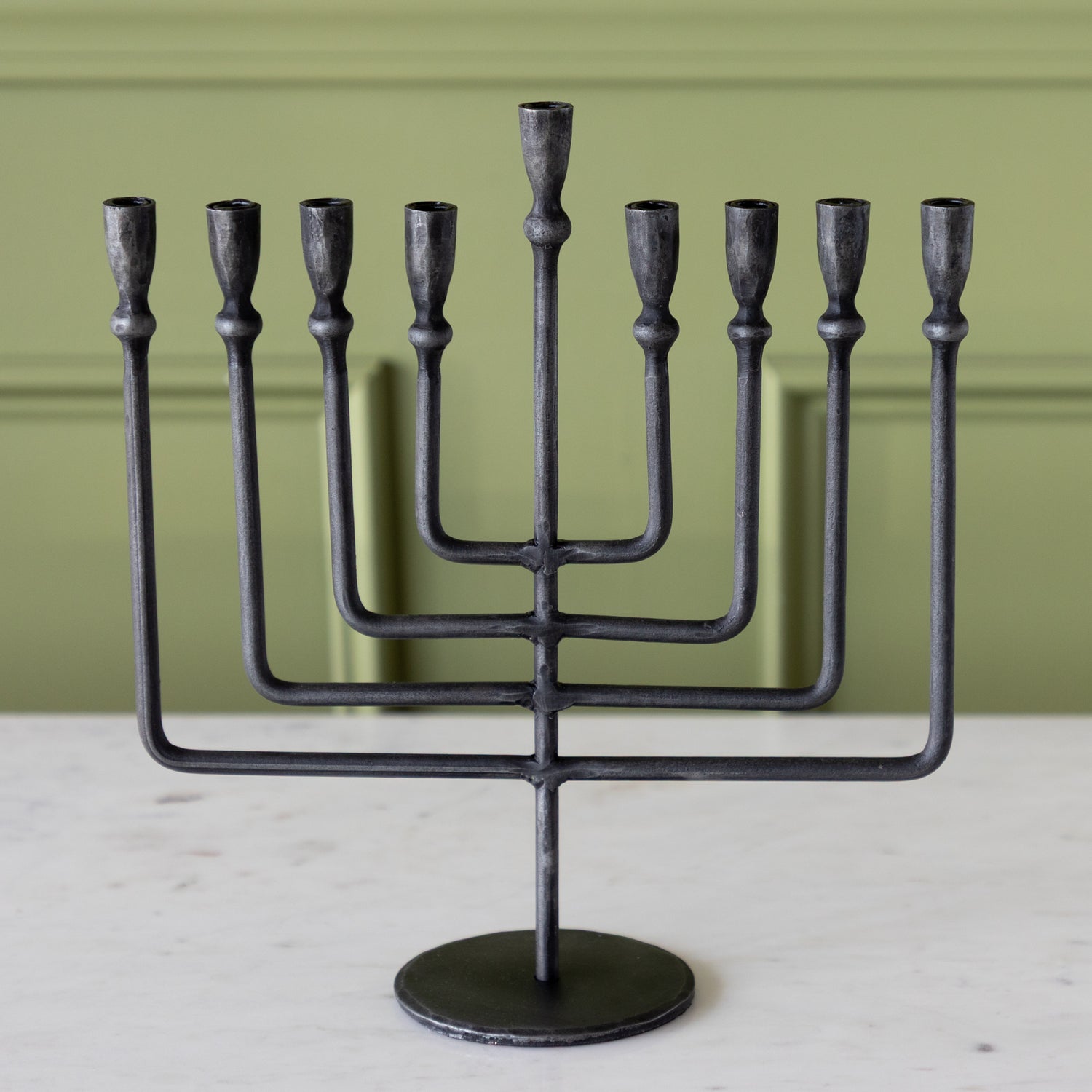 Black metal Menorah on a light surface with a green background.