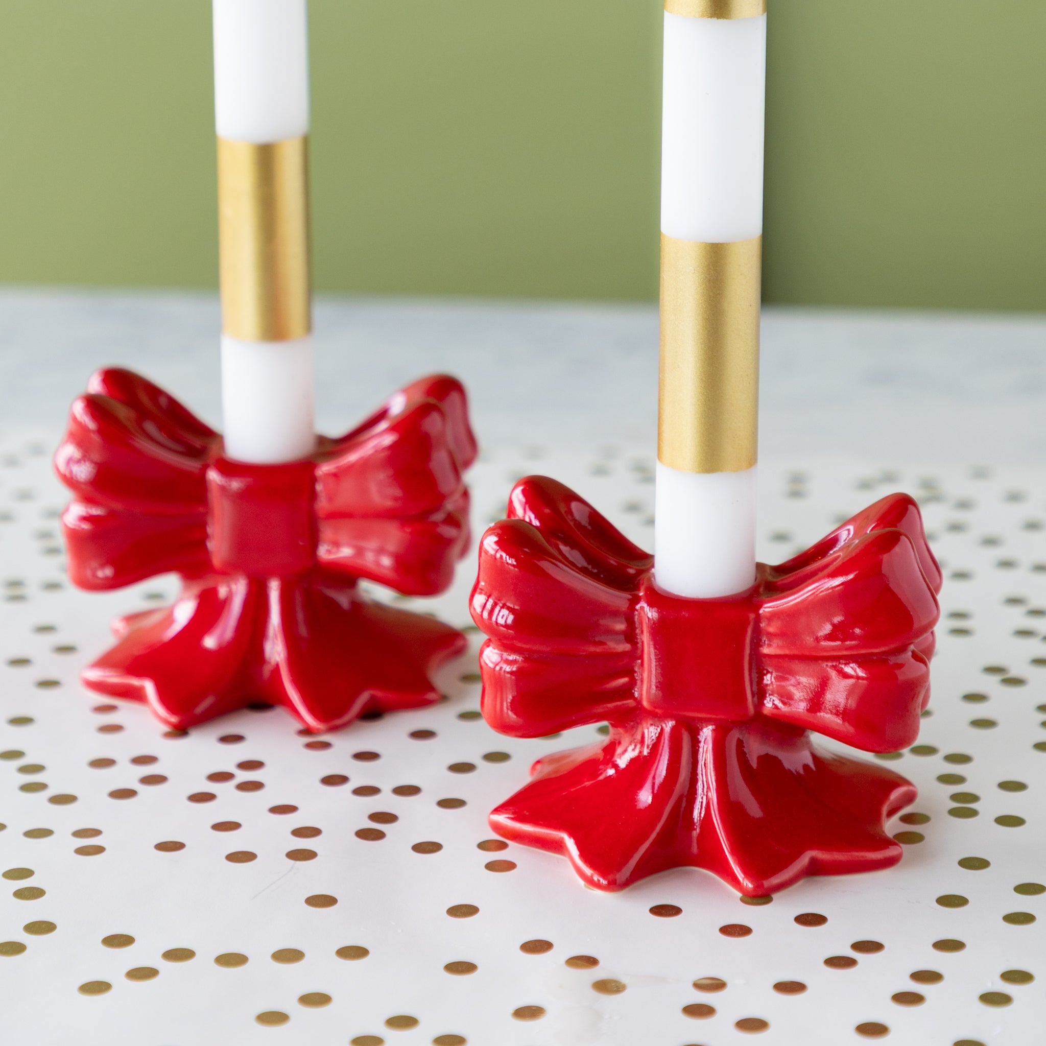 Two red bow-shaped candle holders with white candles on the Gold Confetti Runner.