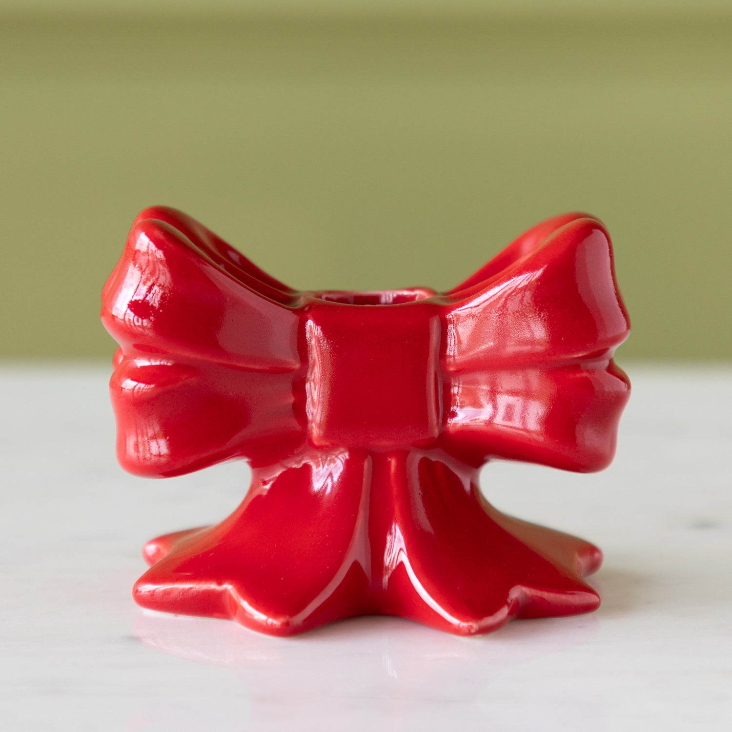 Red ceramic bow-shaped taper candle holder on a white surface with a green background