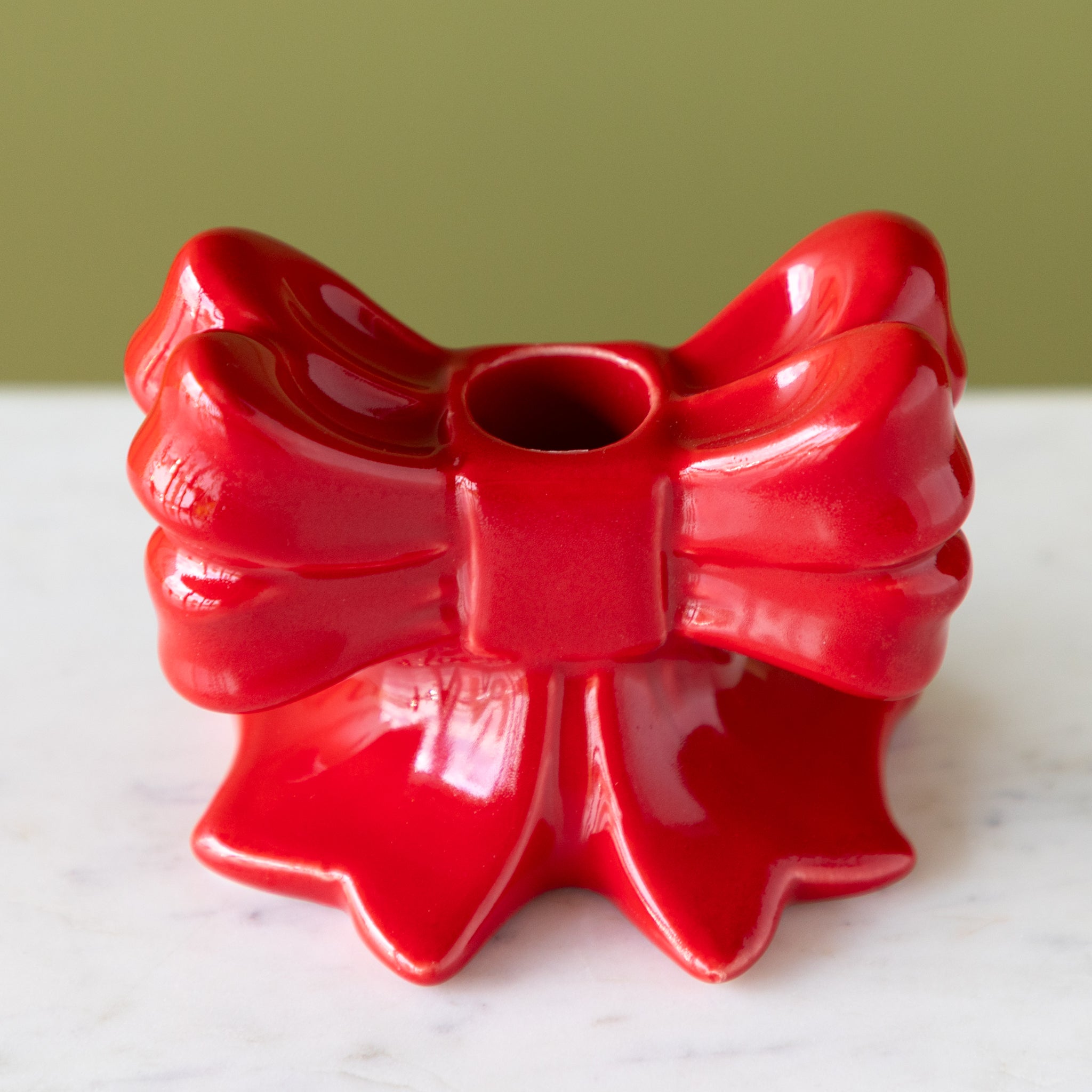 Red bow-shaped taper candle holder on a white surface with a green background.