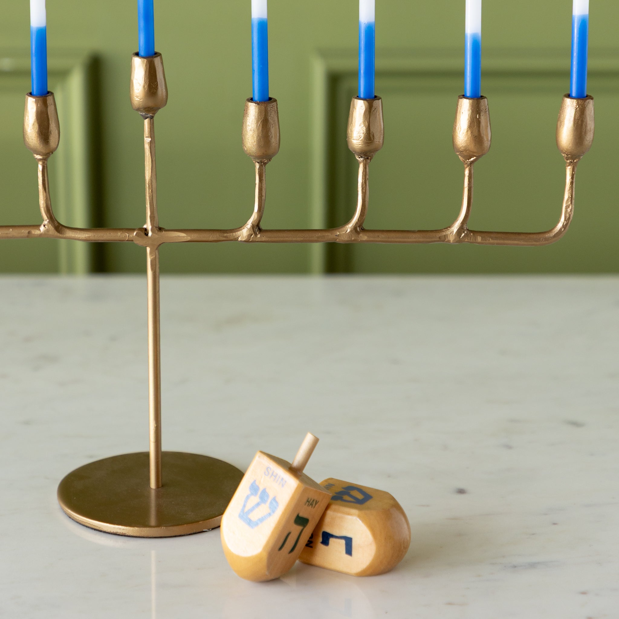Brass menorah with blue candles and a wooden dreidel on a light surface.