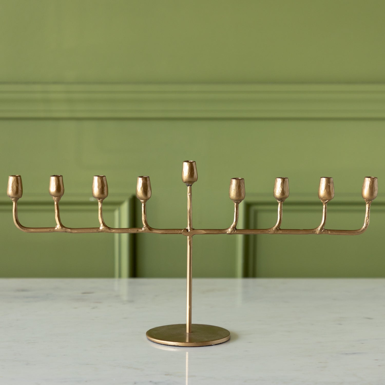 Gold menorah on a marble surface with a green wall background.