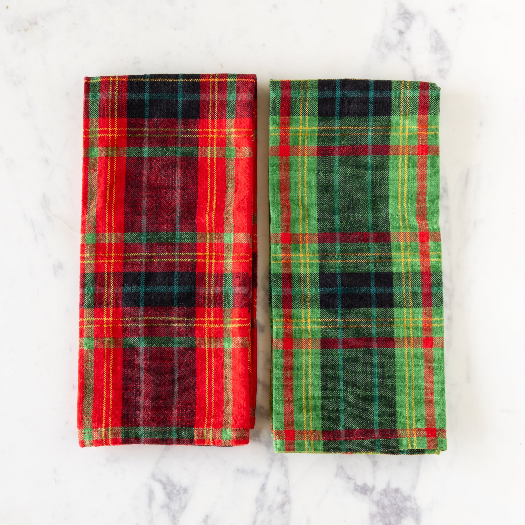 Two plaid towels, one red and green, the other green and red, on a marble surface.