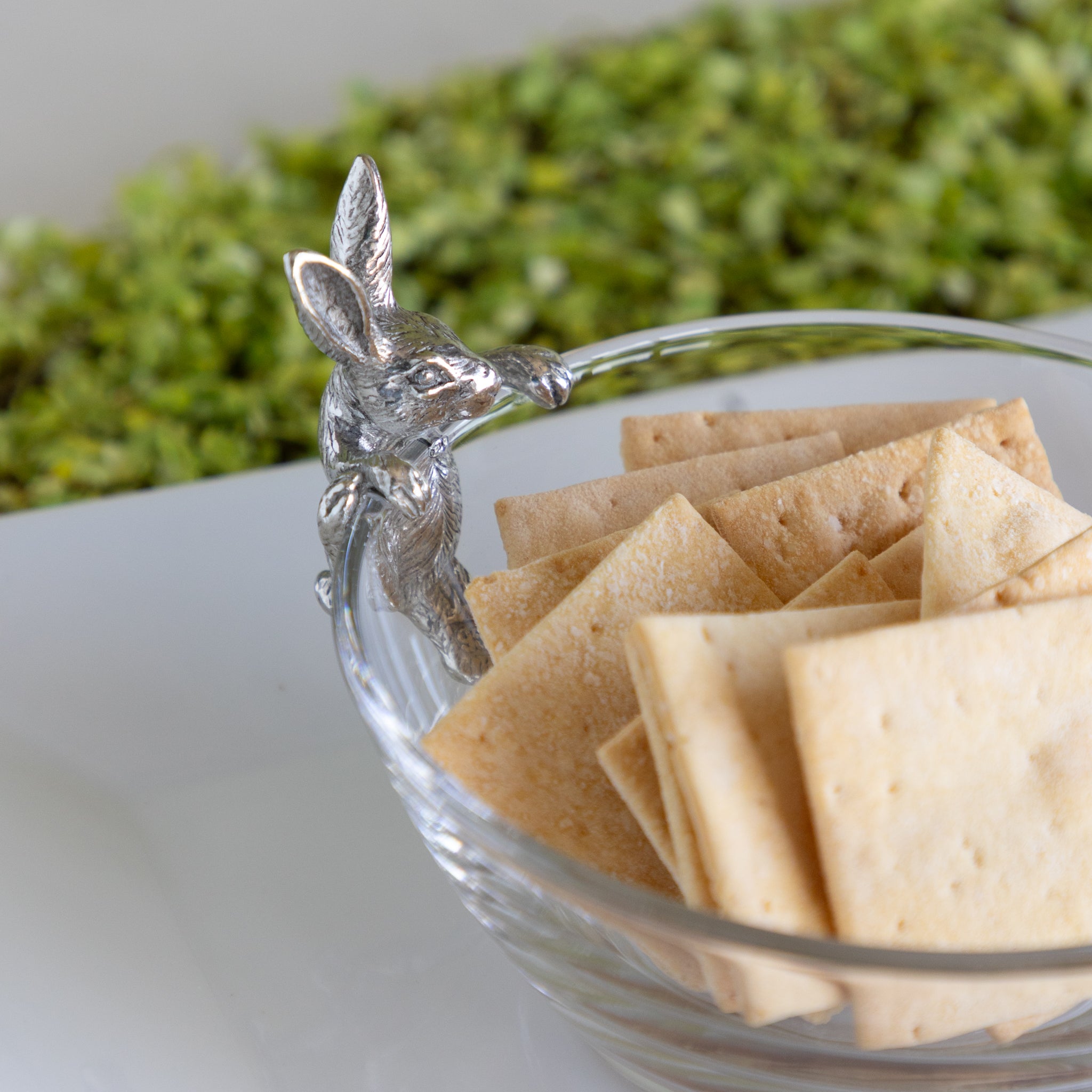 Clear glass bowl with silver rabbit filled with crackers.