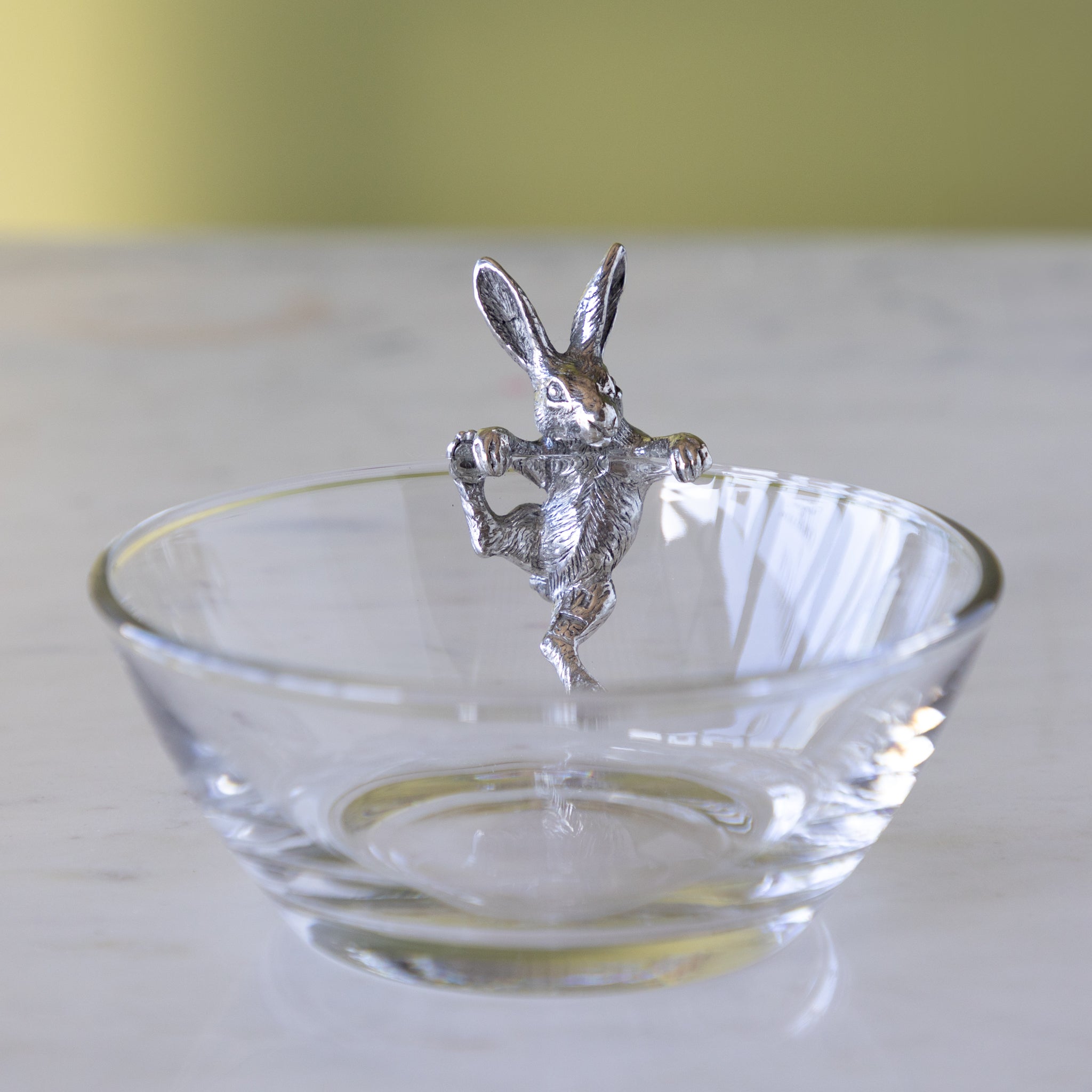 Silver rabbit figurine on a clear glass bowl with a plain background.