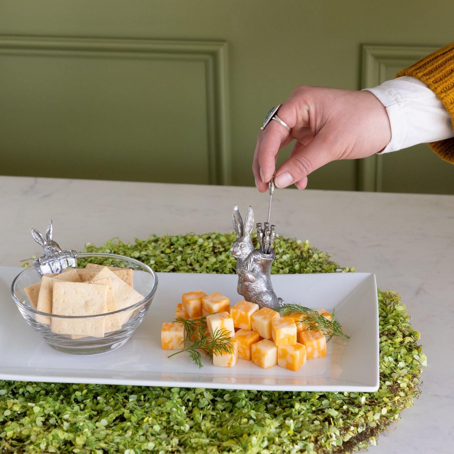 Person grabbing a carrot pick to serve cheese cubes from a platter.