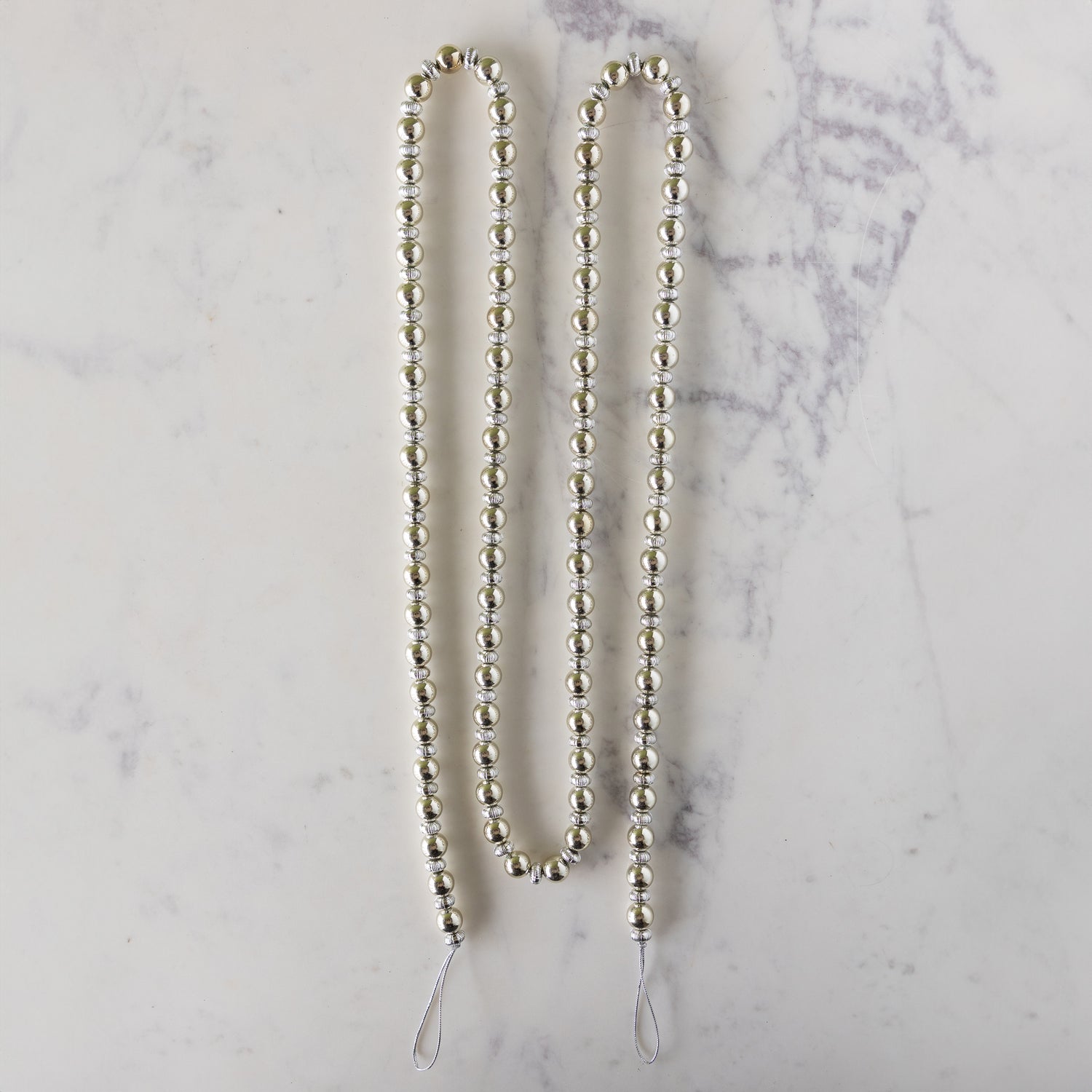 Silver beaded garland on a marble surface.