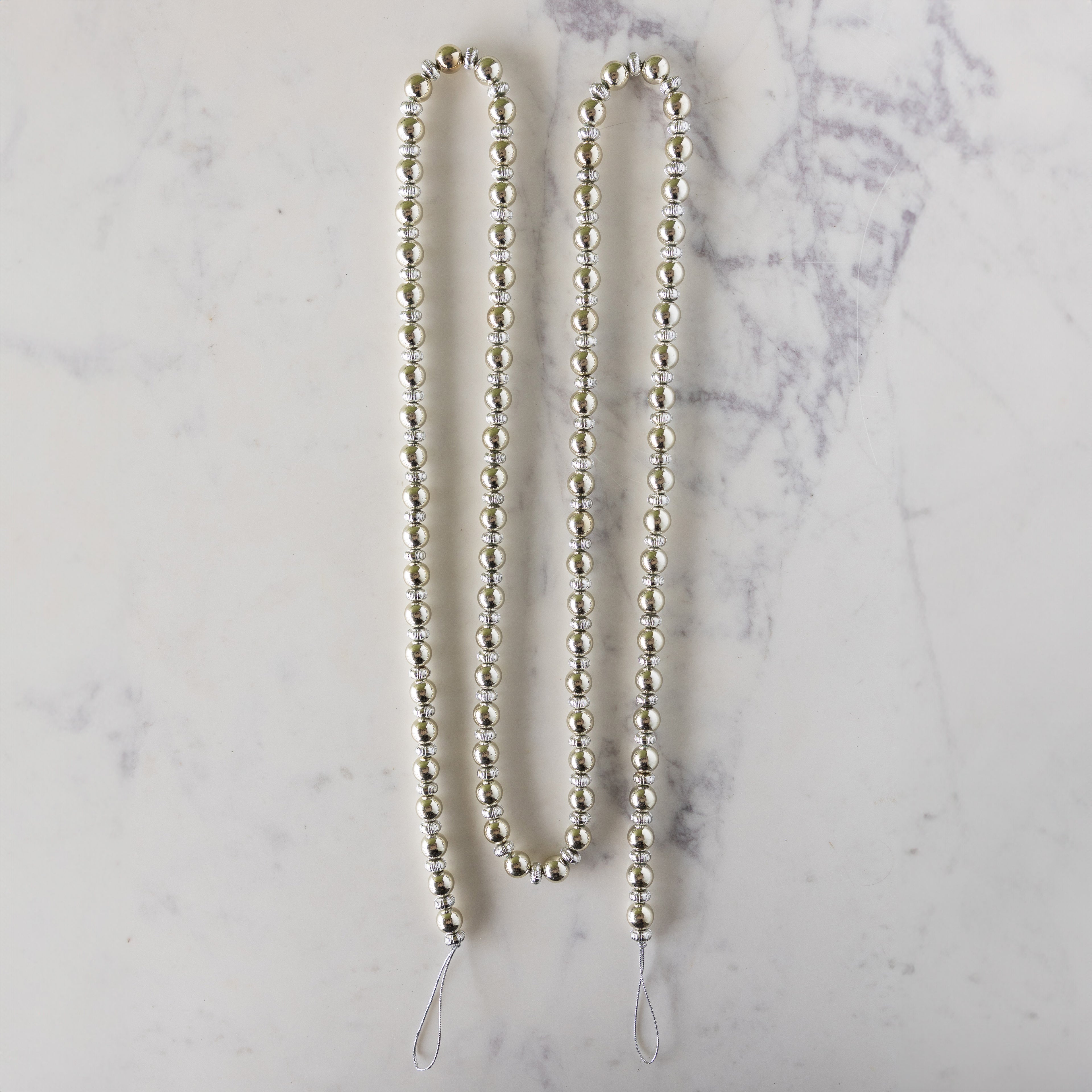 Silver beaded garland on a marble surface.
