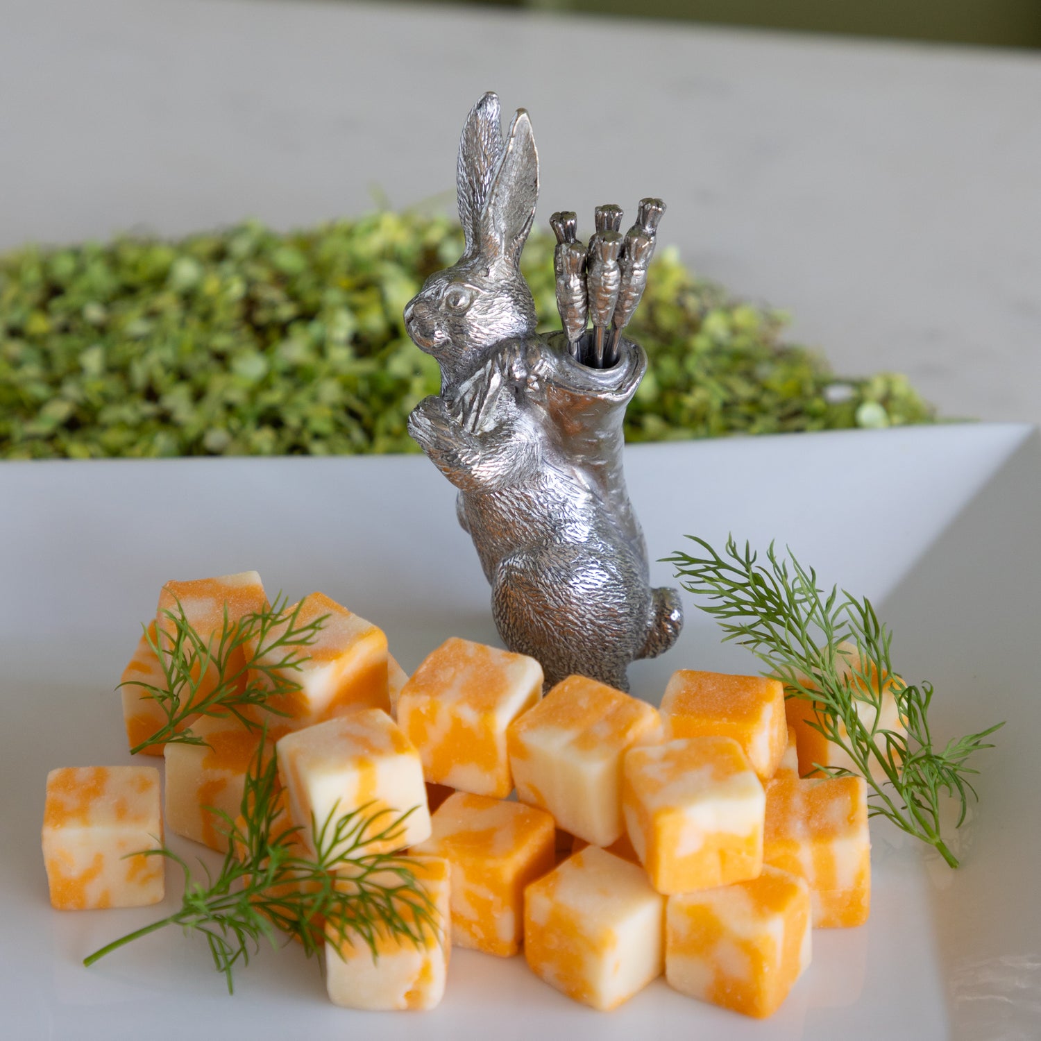 Silver rabbit carrying carrot picks on a platter with cheese cubes.