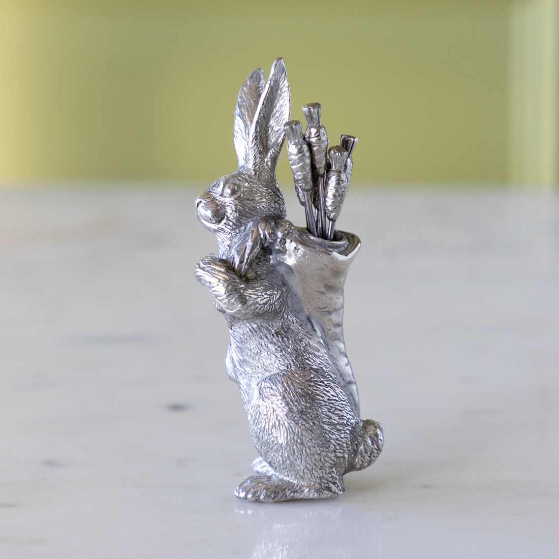 Silver rabbit figurine holding carrot picks on a white surface.