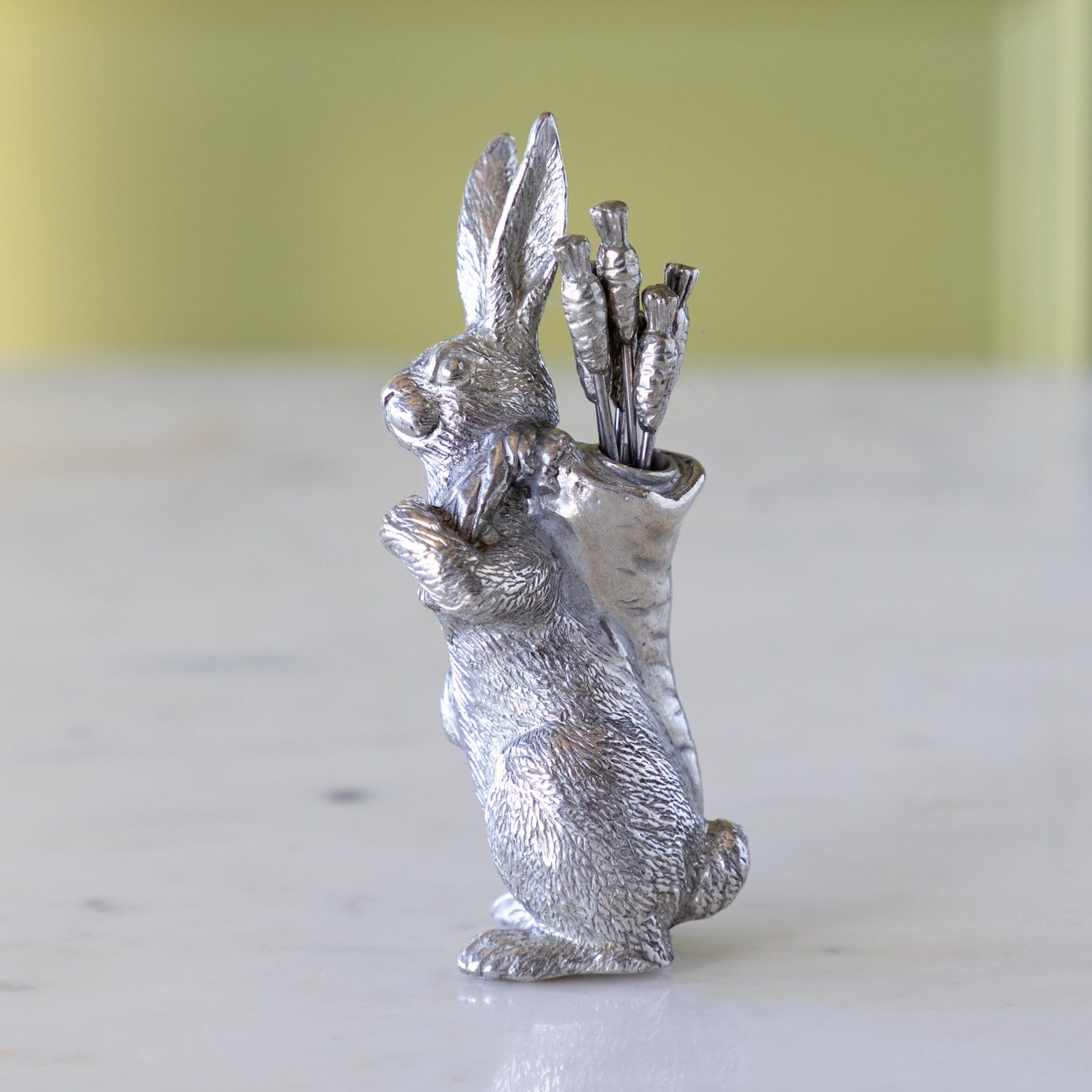 Silver rabbit figurine holding carrot picks on a white surface.
