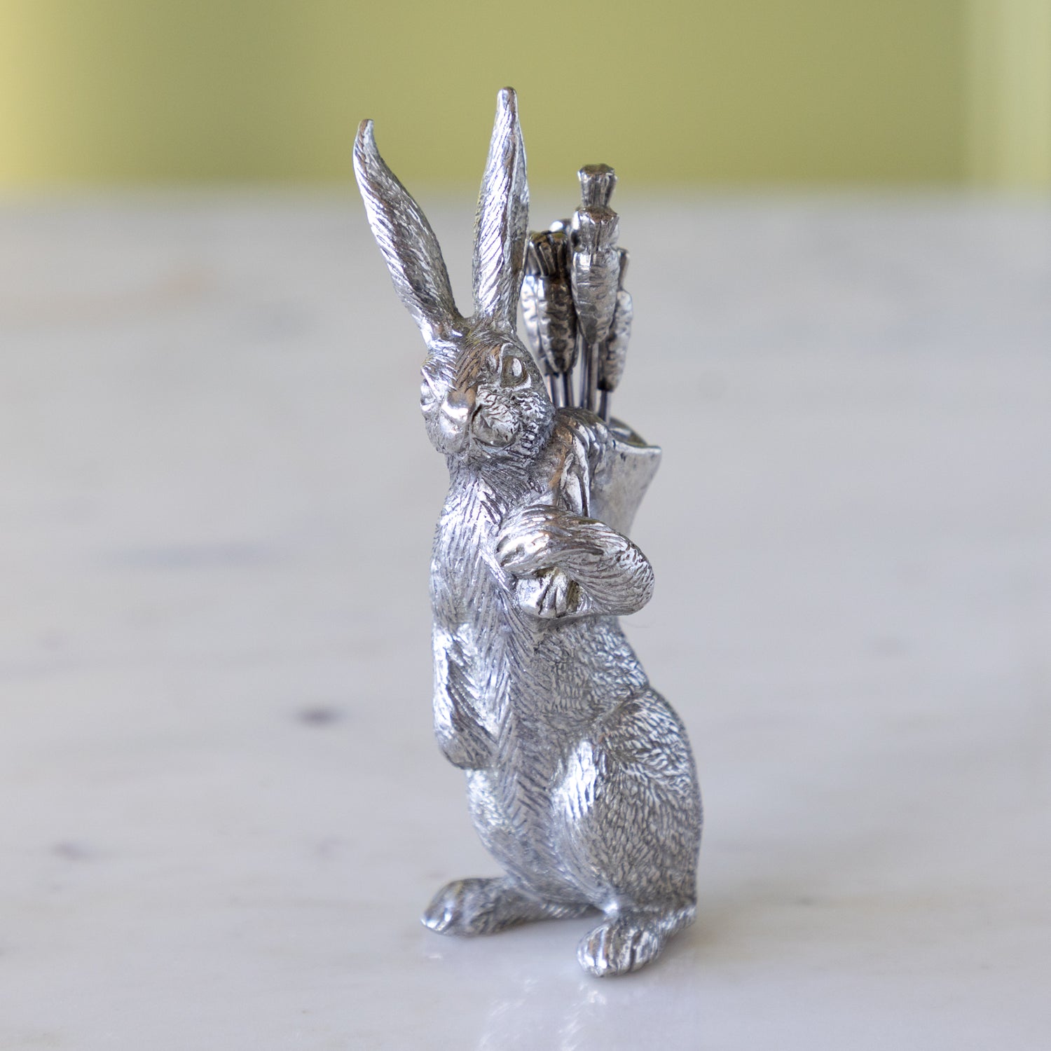 Silver rabbit figurine holding carrot picks on a marble surface.