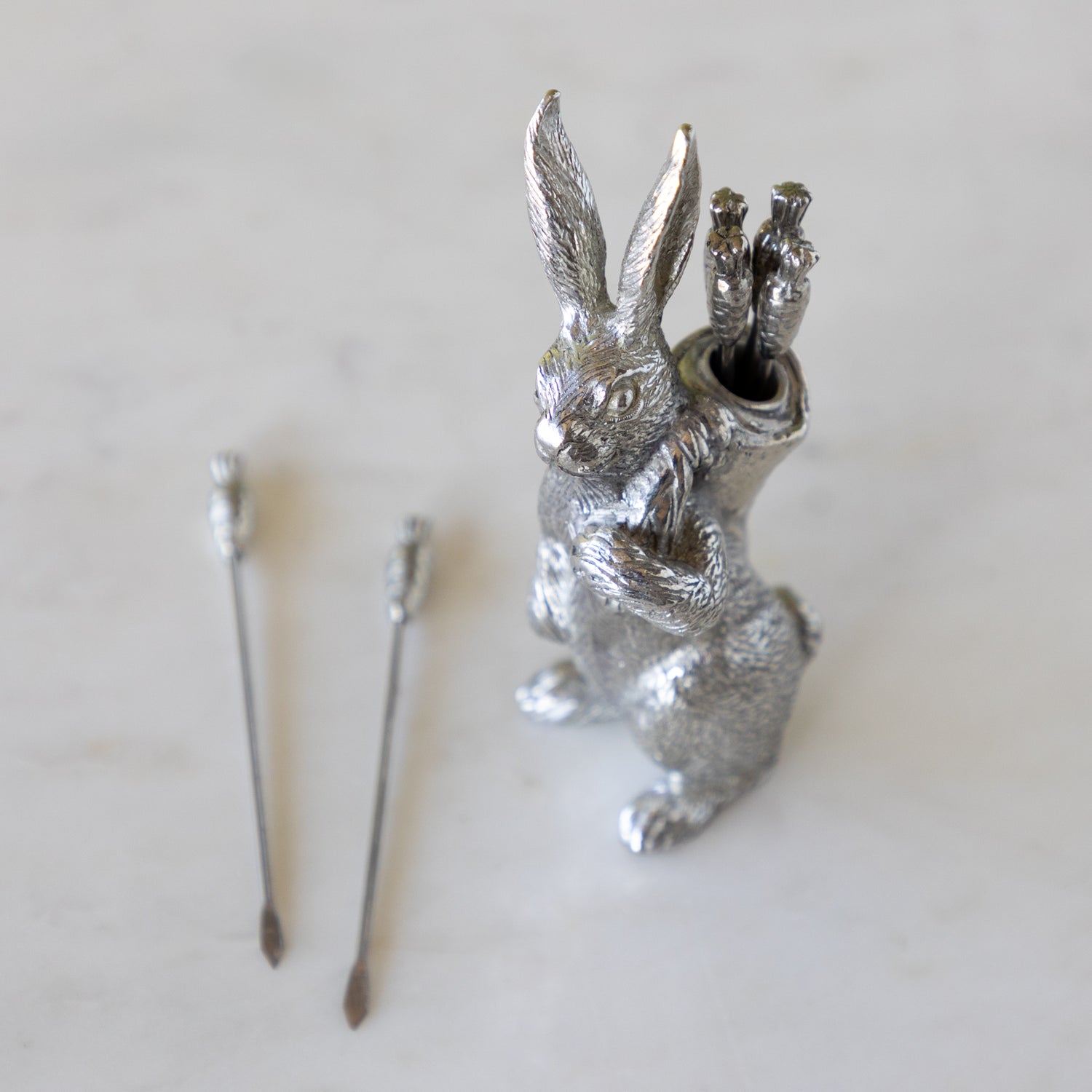 Silver rabbit with carrot picks on a marble table.