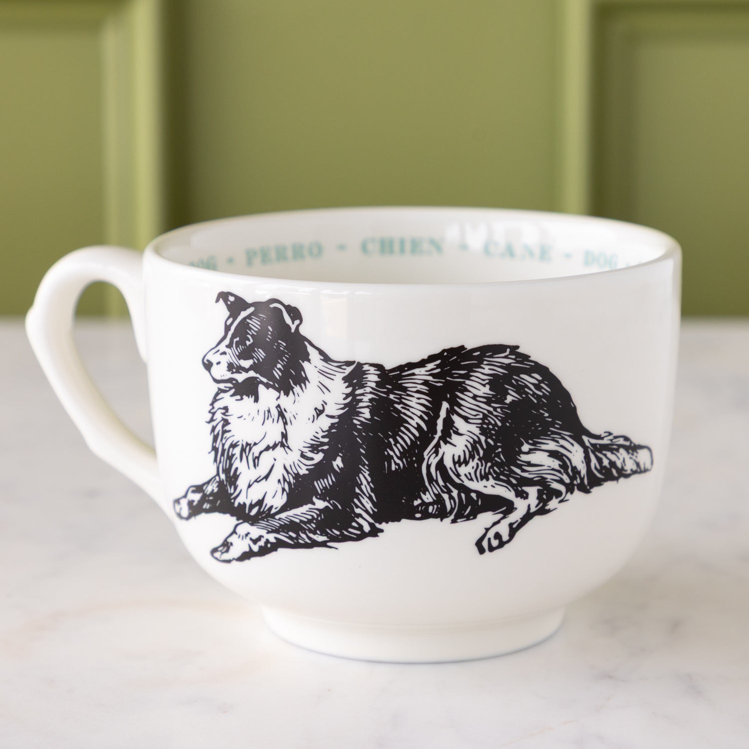 White mug with black dog illustration with &quot;dog&quot; in different languages in light blue text around the inside rim.
