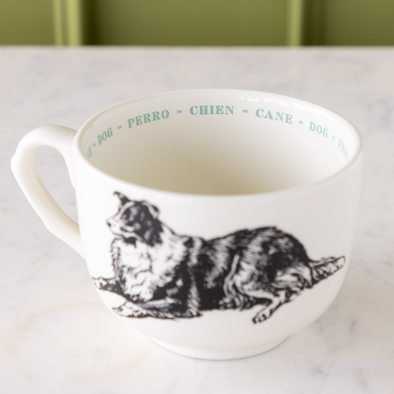 White mug with black dog illustration with &quot;dog&quot; in different languages in blue ext around the inside rim.