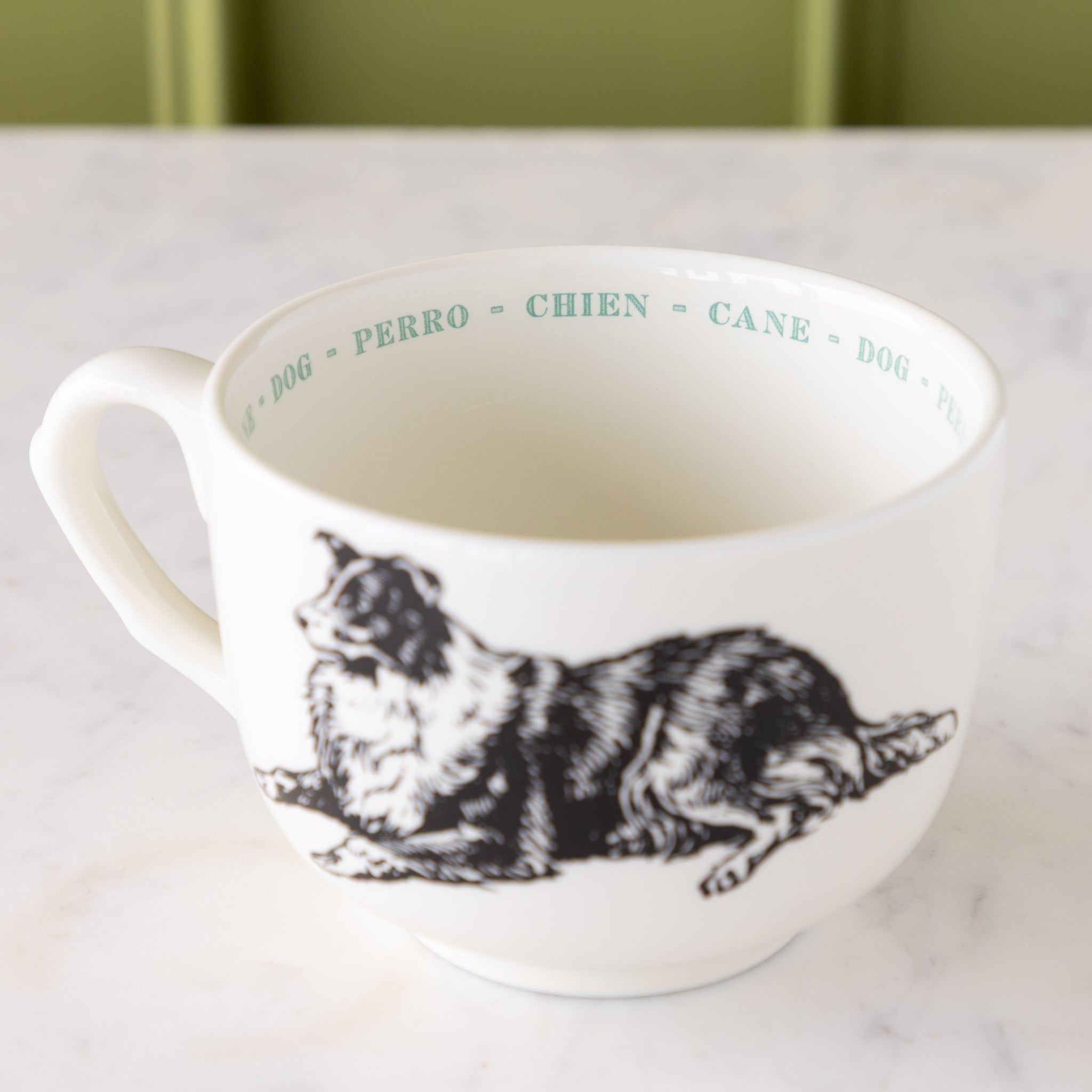 White mug with black dog illustration with &quot;dog&quot; in different languages in blue ext around the inside rim.