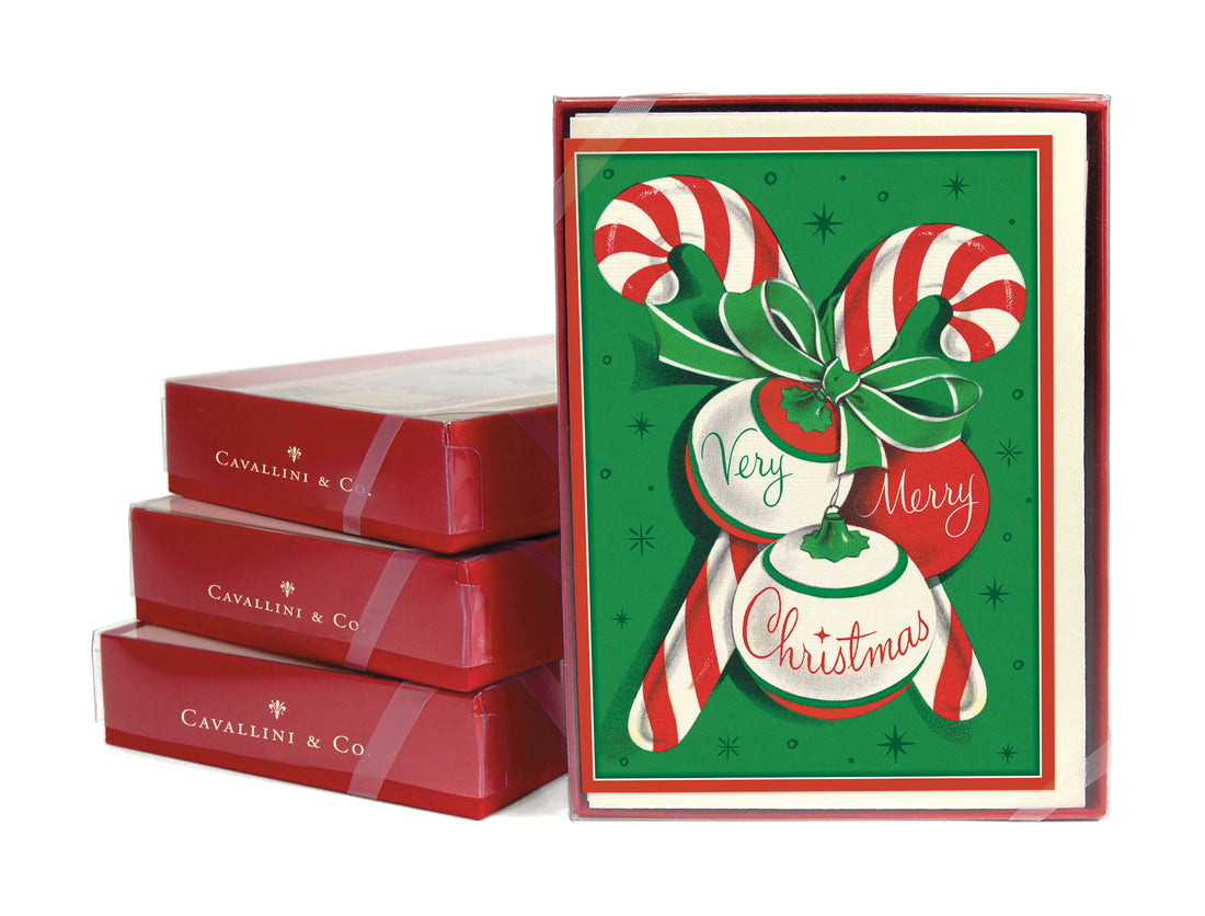 A stack of three boxed set cards next to a front facing card set of the Candy Canes Christmas Card Set showing two candy canes crossed with a bow tying them together and three ornaments with the words &quot;very&quot;, &quot;merry&quot; and &quot;Christmas&quot; on them.