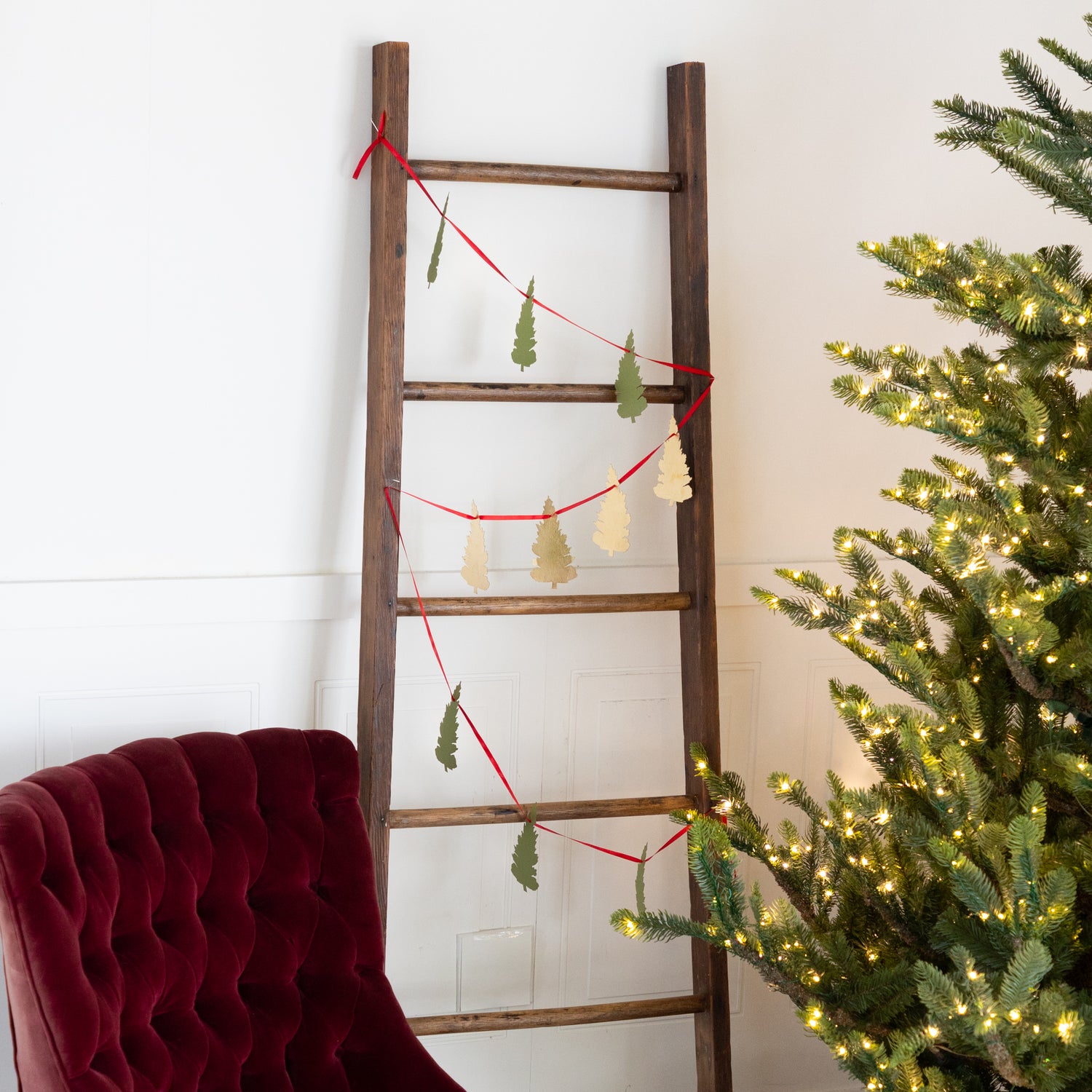 Wooden ladder with Christmas decorations next to a decorated tree and red chair.