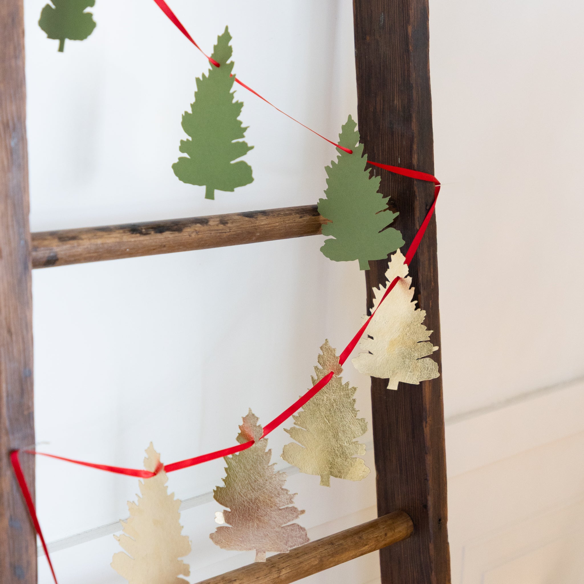 Decorative ladder with paper tree cutouts and red string on a white background.