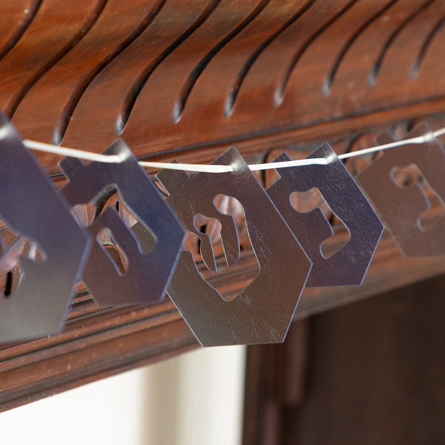 Decorative dreidel shaped cutouts on a string against a wooden background.