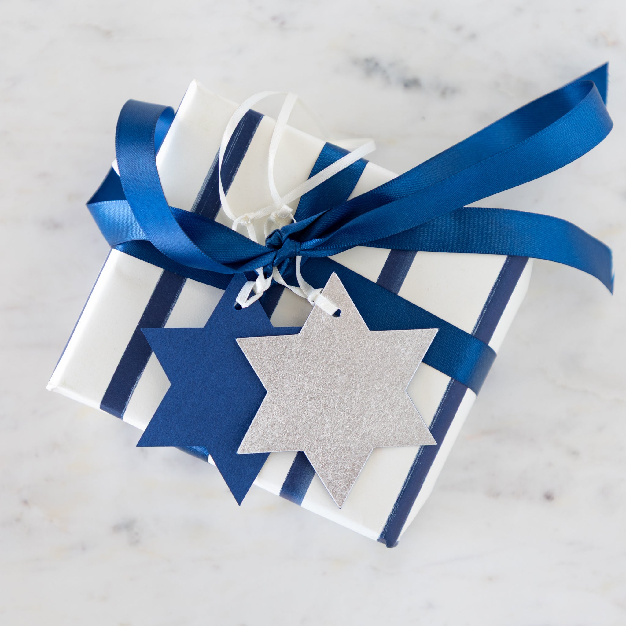 Gift box wrapped in blue and white with a Star of David tag on a marble surface.