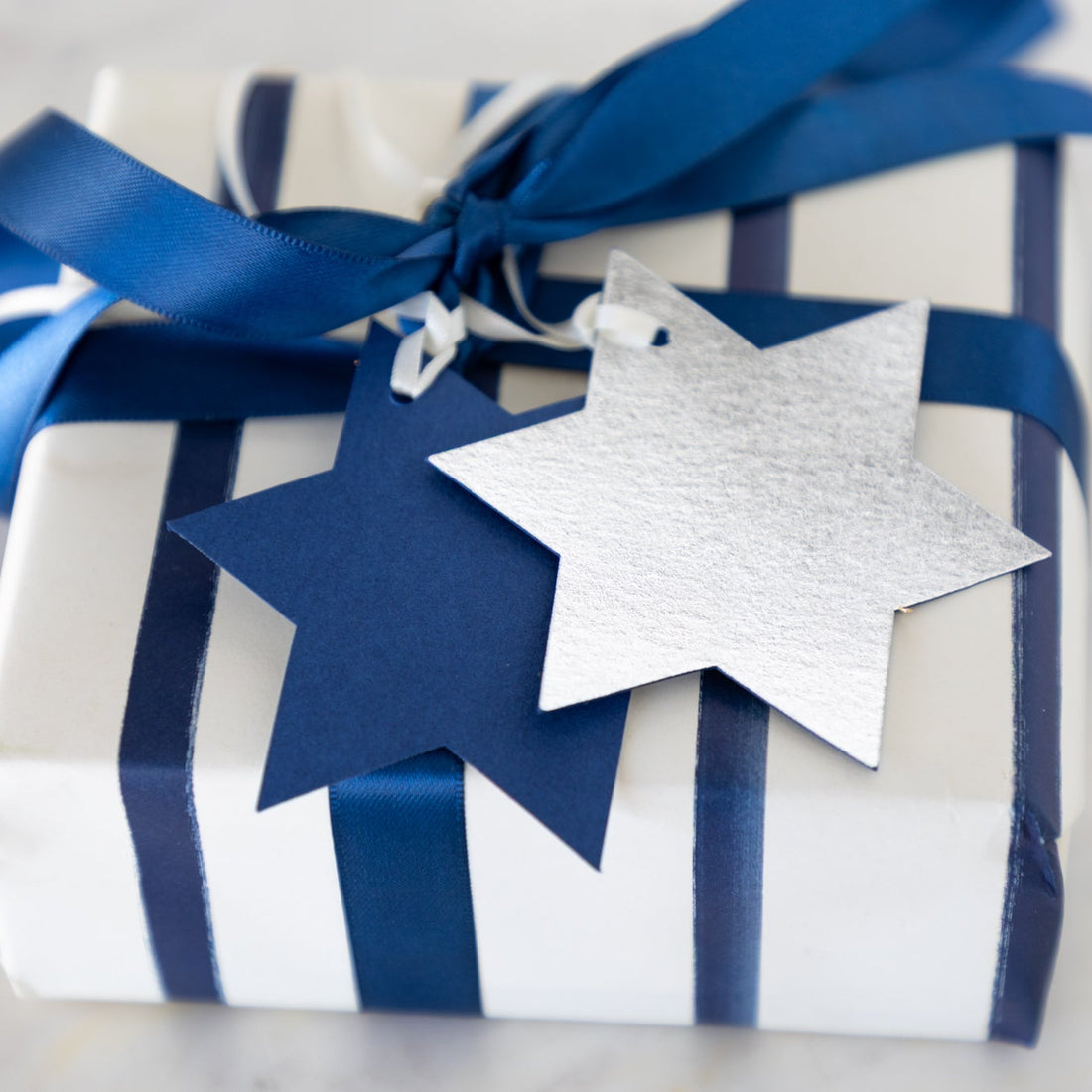 Gift wrapped in blue and white stripes with a Star of David tag on a neutral background.
