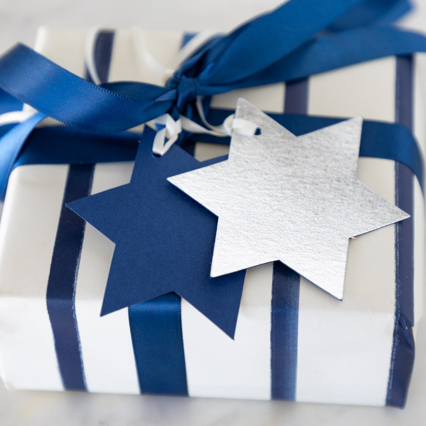 Gift wrapped in blue and white stripes with a Star of David tag on a neutral background.