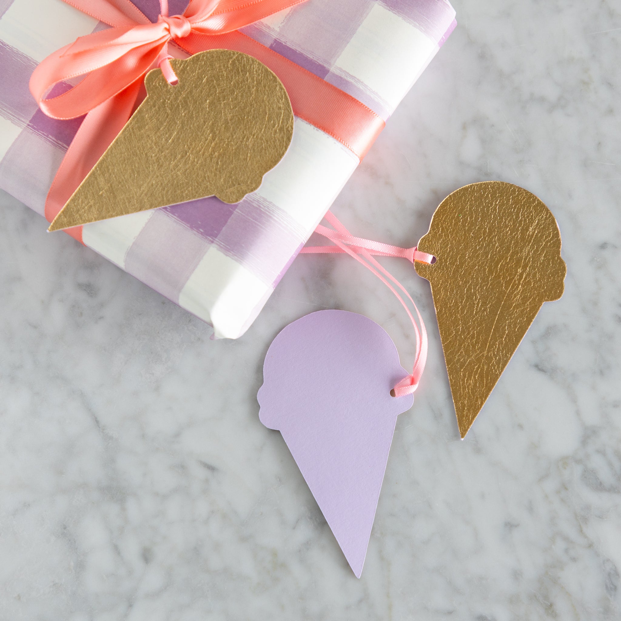 Reversible gold-foiled and purple ice cream cone gift tags on a marble surface with a wrapped gift in the background.