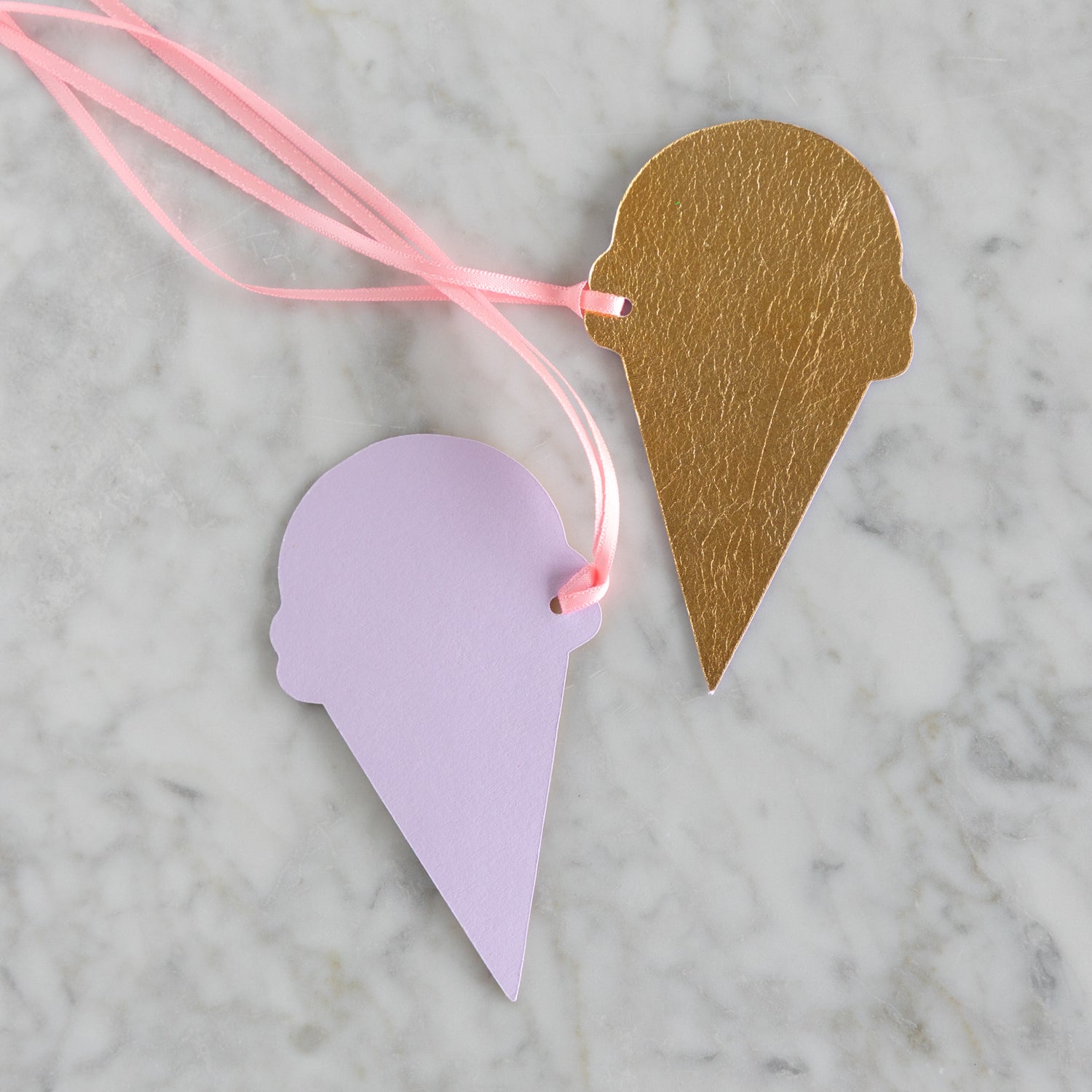 One gold-foiled ice cream cone tag showing the front and a second showing the purple backside on a marble surface.