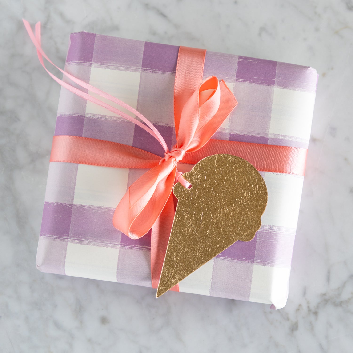 Gift box with purple and white checkered pattern, pink ribbon, and gold-foiled ice cream cone gift tag on a marble background.
