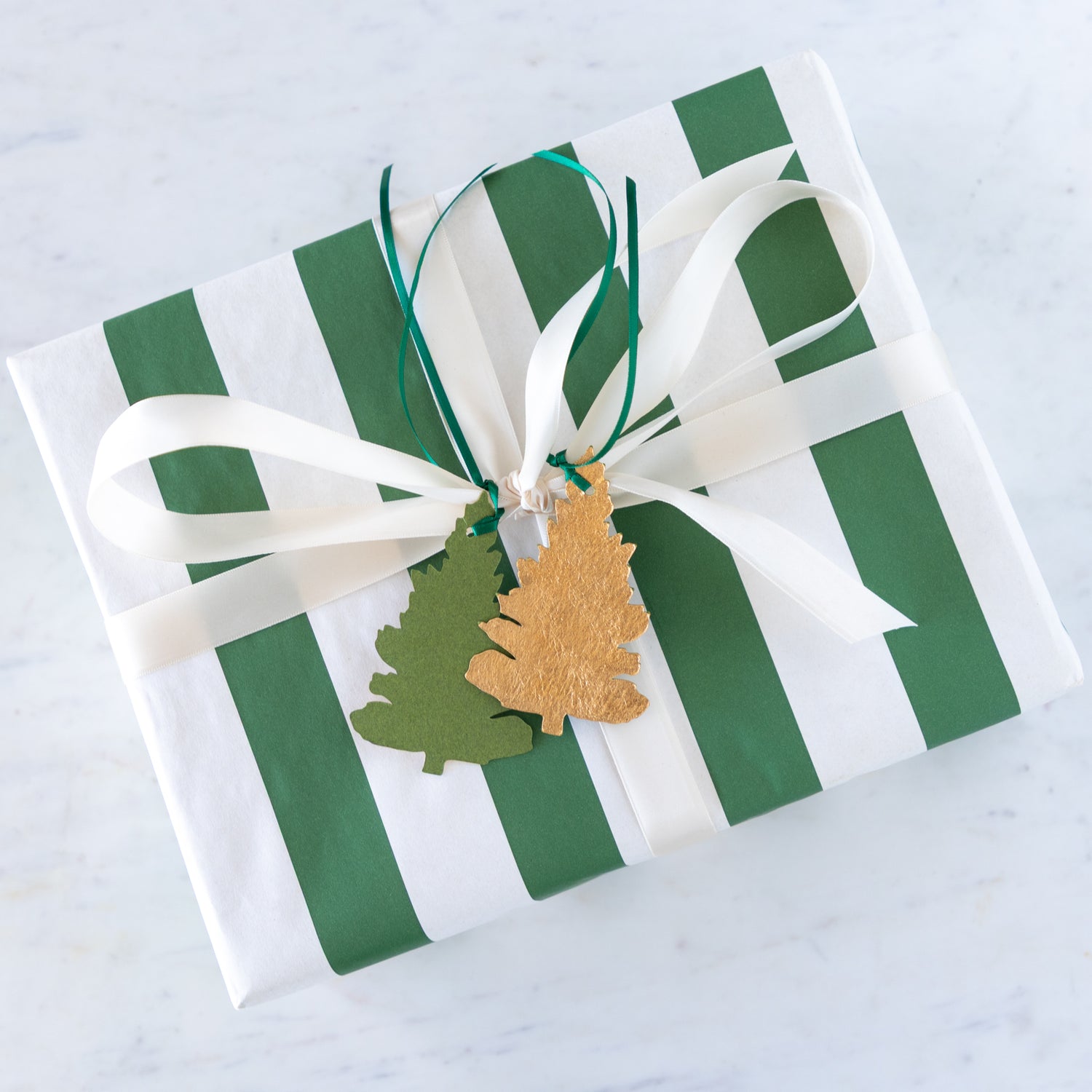 Gift box with green and white striped pattern, white ribbon, and decorative tags on a light gray background.