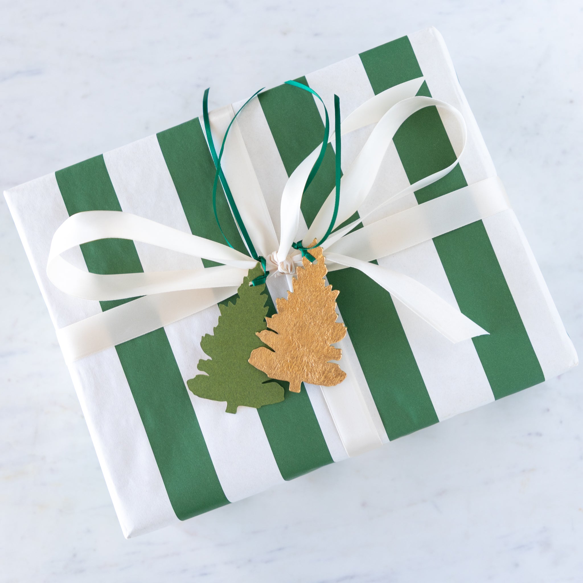 Gift box with green and white striped pattern, white ribbon, and decorative tags on a light gray background.