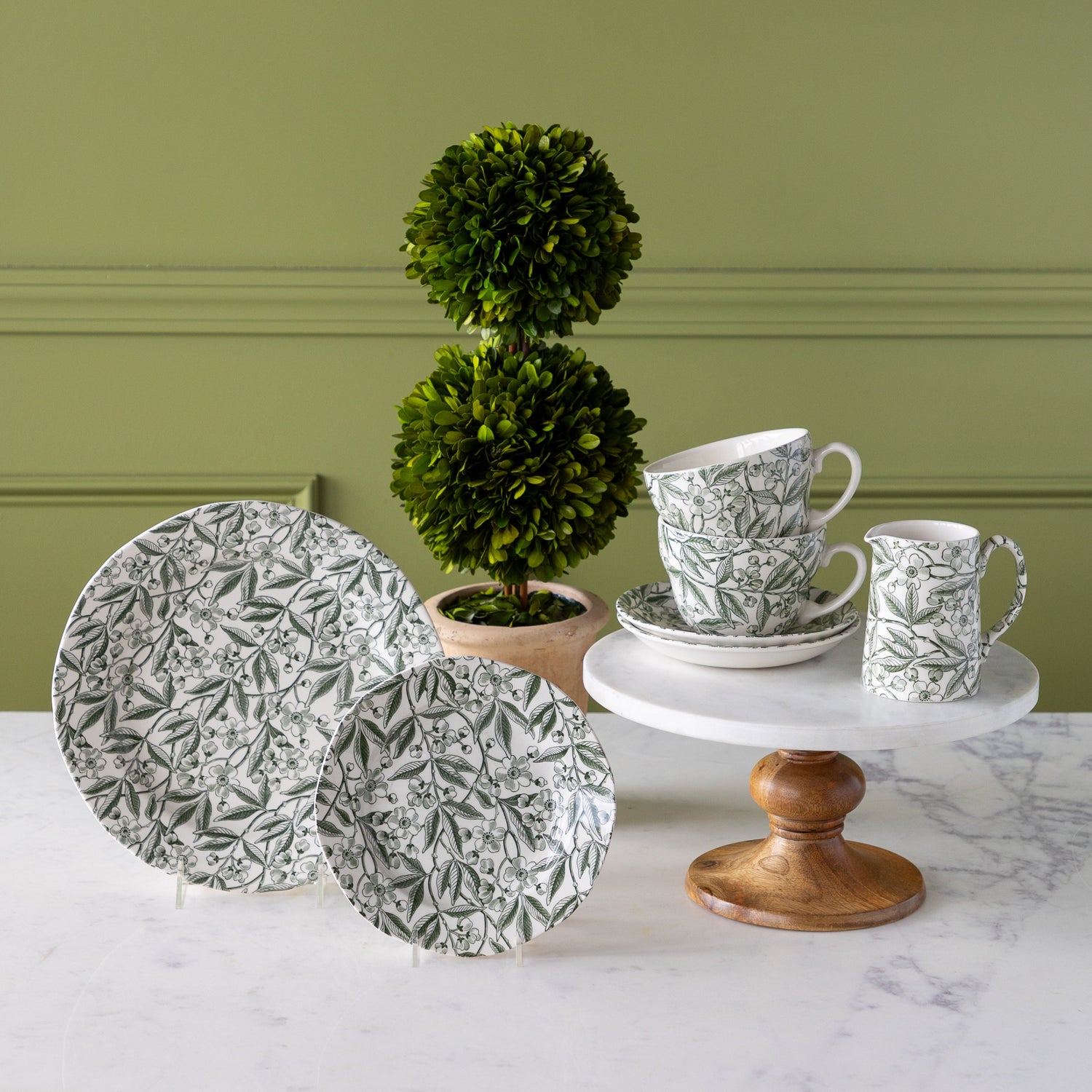 Burleigh Green Prunus Dinnerware propped on pedestals with a topiary plant in the background.