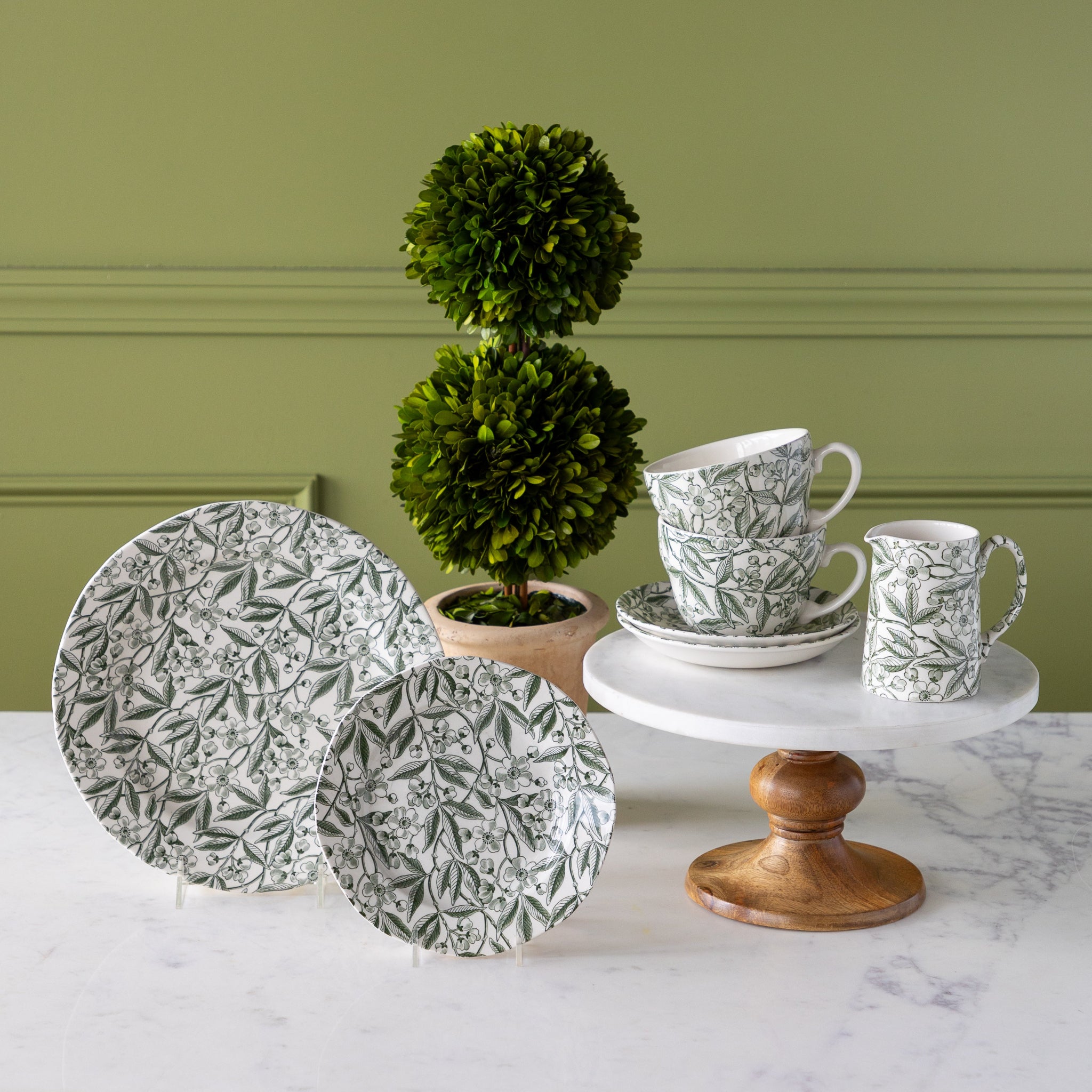 Burleigh Green Prunus Dinnerware propped on pedestals with a topiary plant in the background.