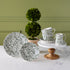 Burleigh Green Prunus Dinnerware propped on pedestals with a topiary plant in the background.