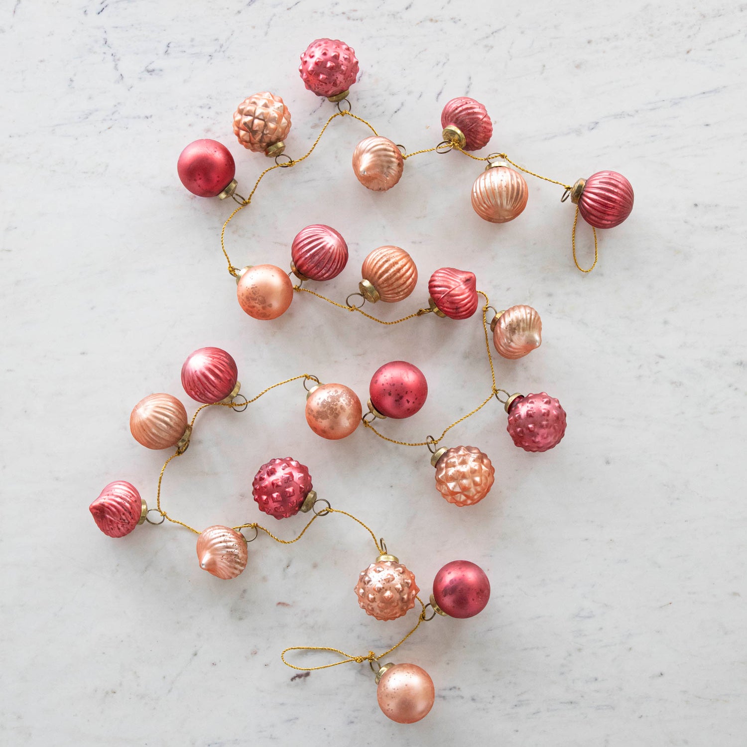 Embossed Mercury Glass Ball Ornament Pink Garland on a marble table.