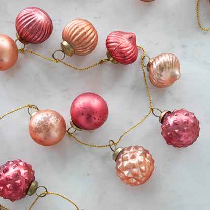 Close up view of the Embossed Mercury Glass Ball Ornament Pink Garland showing various pinks and details in the ornaments strung on a gold jute cord.