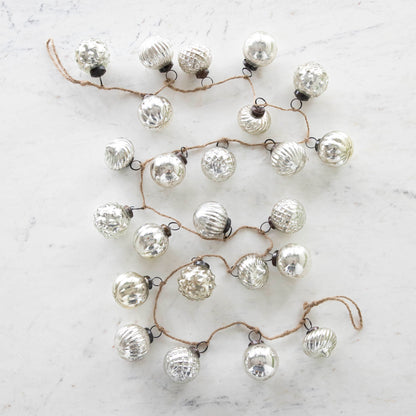 Silver Embossed Mercury Glass Ornament Garland with a jute cord on a marble table.