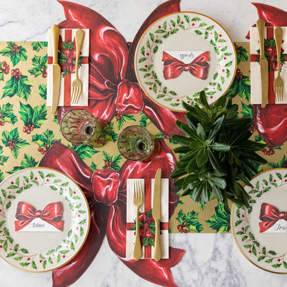 An elegant Christmas themed table setting for three, with the Bow Place Card resting on holly dinner plates on top of the Christmas Bow Placemat with the Gilded Holly Runner underneath.