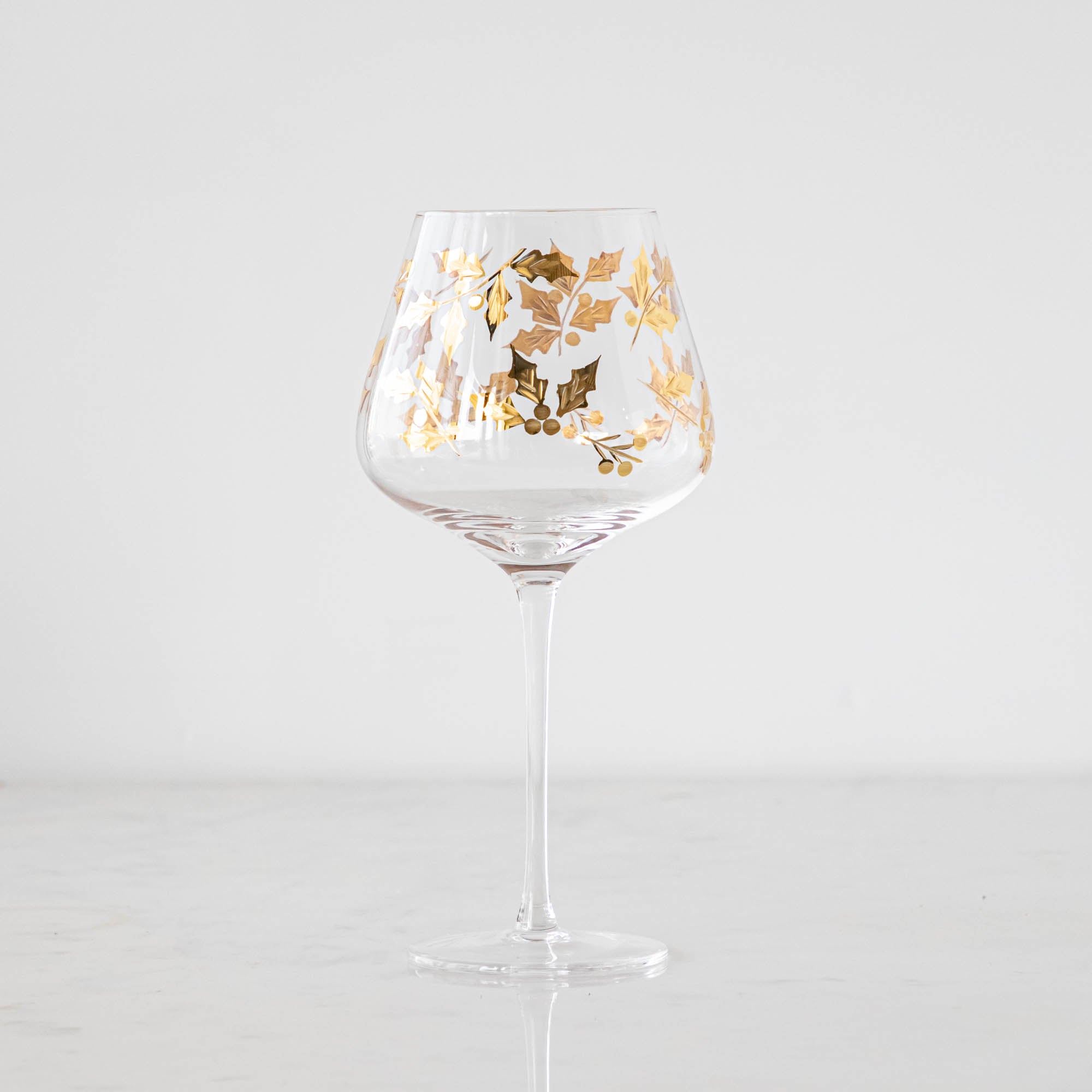 A Gold Holly Etched Goblet on a marble table.