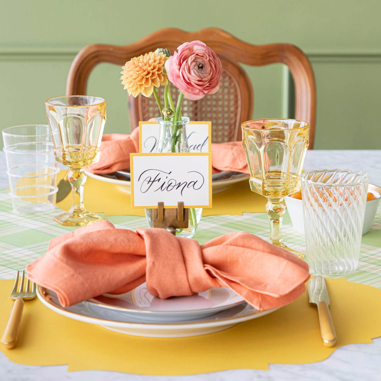 Elegant table setting with pink napkins, glassware, and floral centerpieces on a green tablecloth.