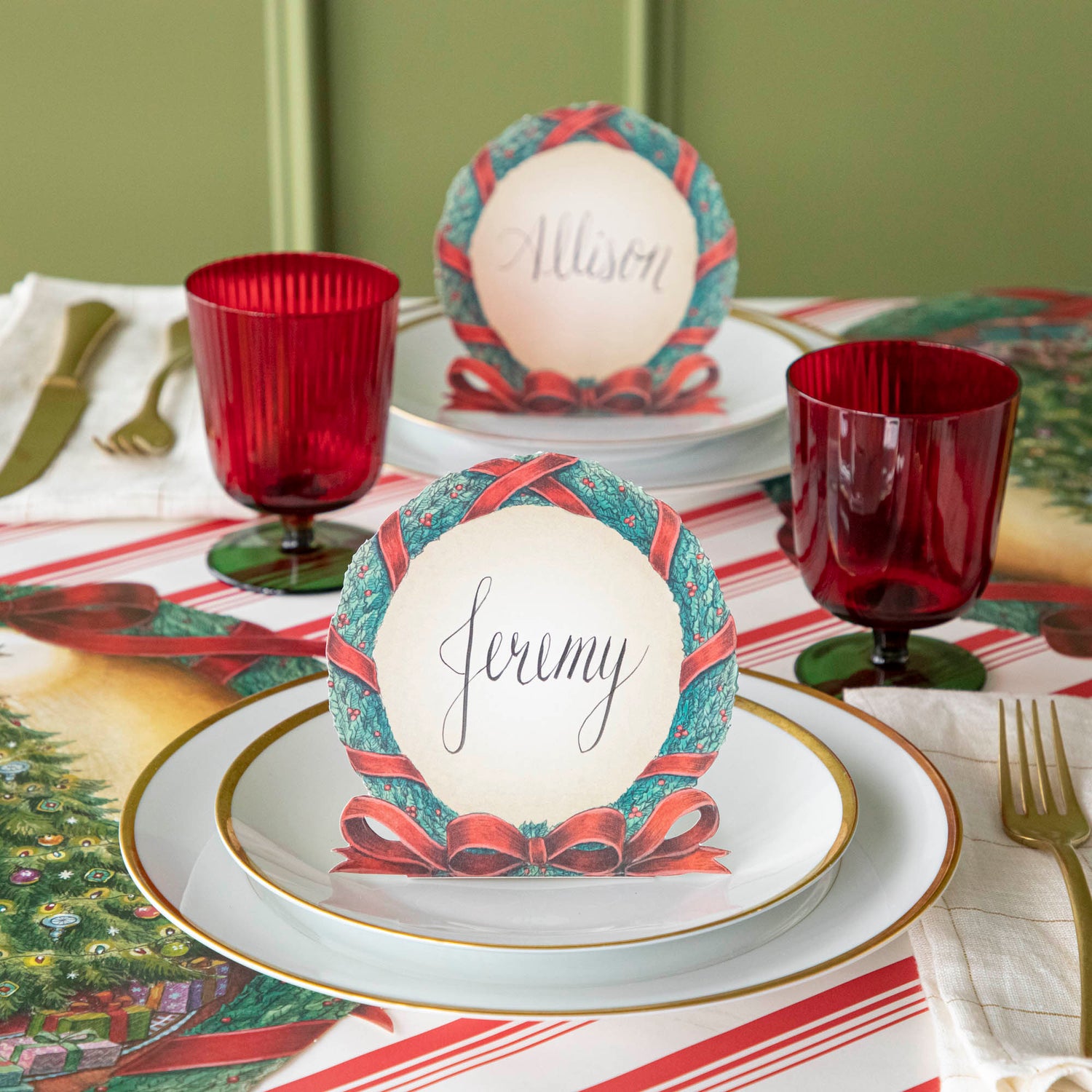 A Christmas wreath place card with the name &quot;Jeremy&quot; written on it on a Christmas themed table.