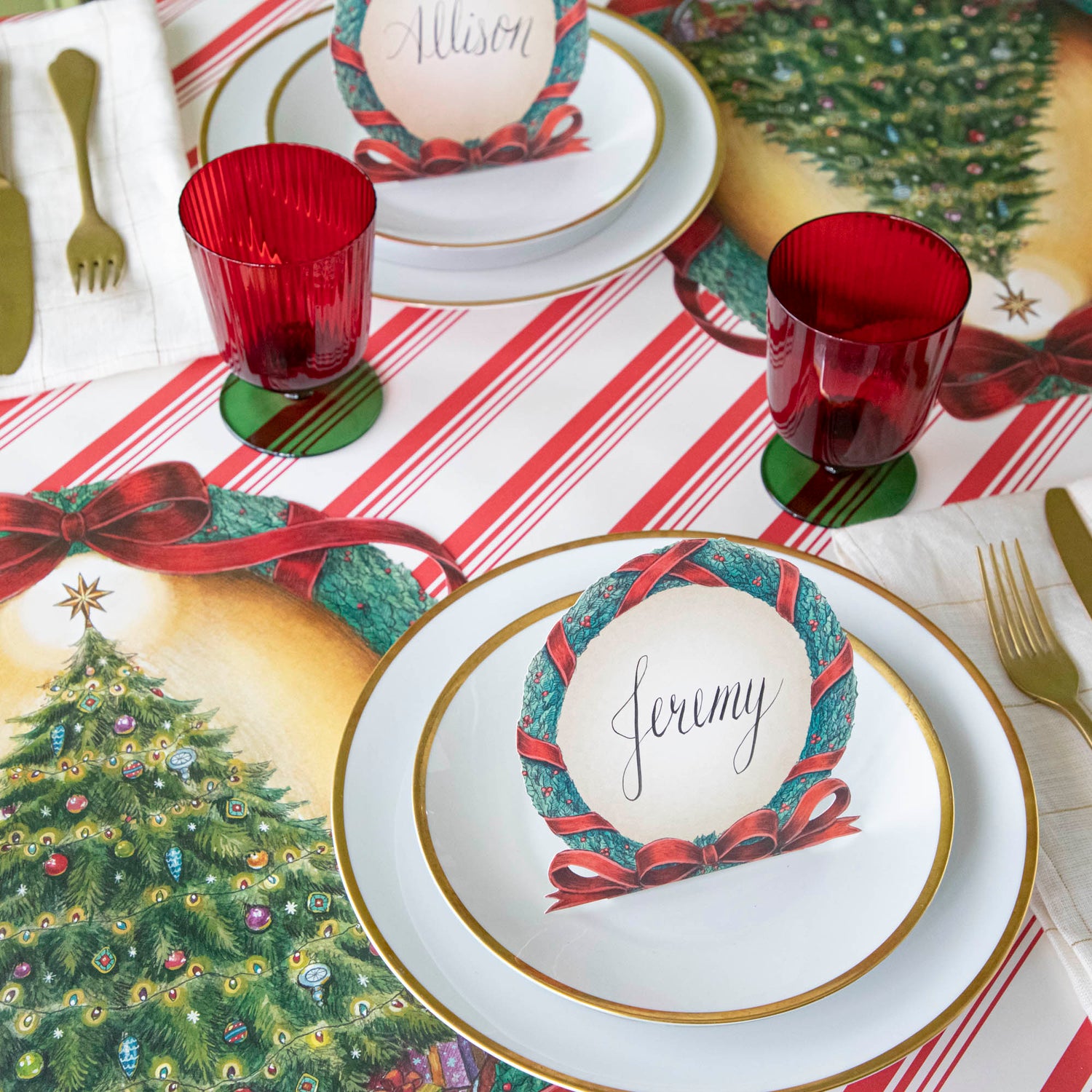 A Christmas themed table setting with plates, silverware and red &amp; green stemmed flute glasses.