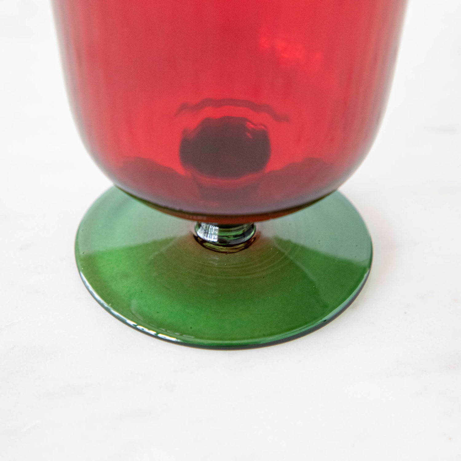 Close up of a green &amp; red stemmed flute glass bottom on a marble table.