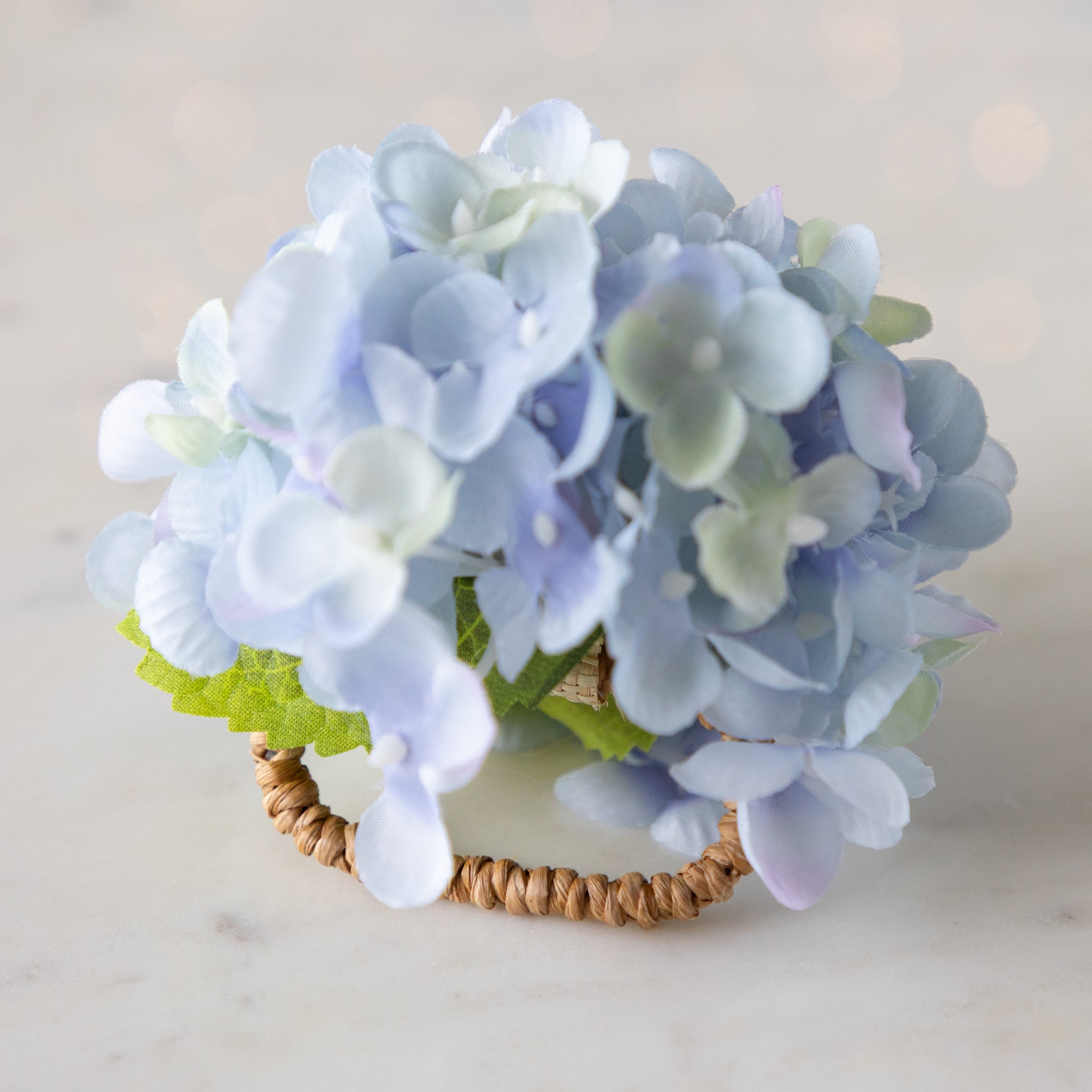 Pastel blue and green flower Hydrangea Napkin Ring with a rattan loop on a marble surface.