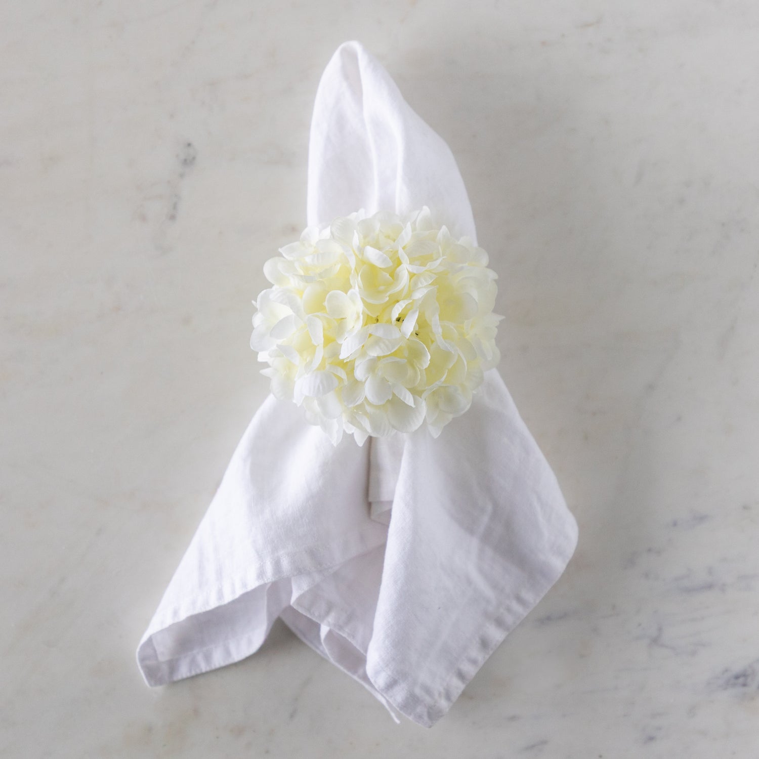 White napkin with a cream Hydrangea Napkin Ring around it, on a marble surface.