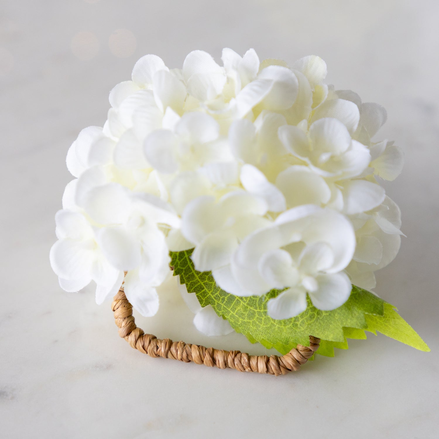 Cream Hydrangea Napkin Ring with a rattan ring on a marble surface.