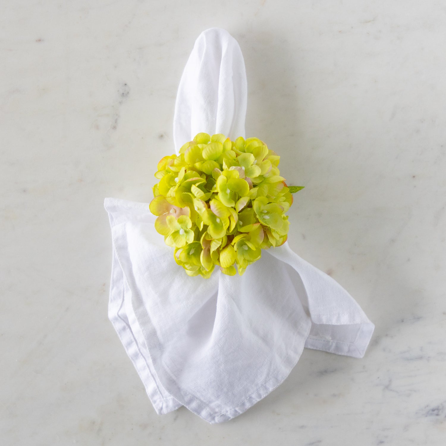 White napkin with a green Hydrangea Napkin Ring around it, on a marble surface.