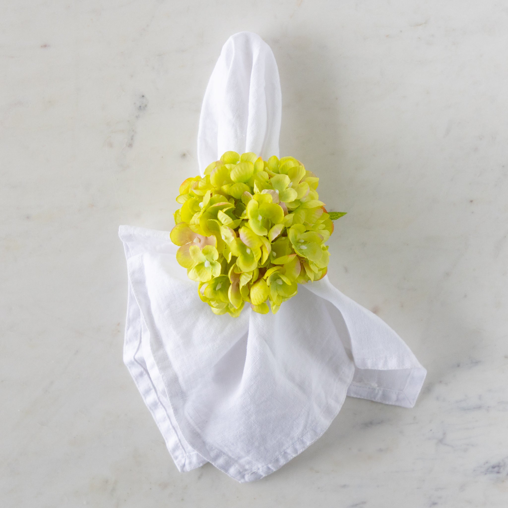 White napkin with a green Hydrangea Napkin Ring around it, on a marble surface.